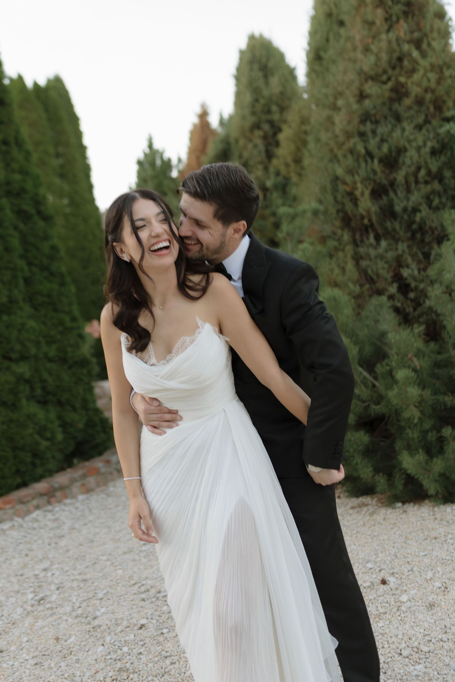 A couple in wedding attire share joyful candid moments together outdoors against a backdrop of evergreen trees.