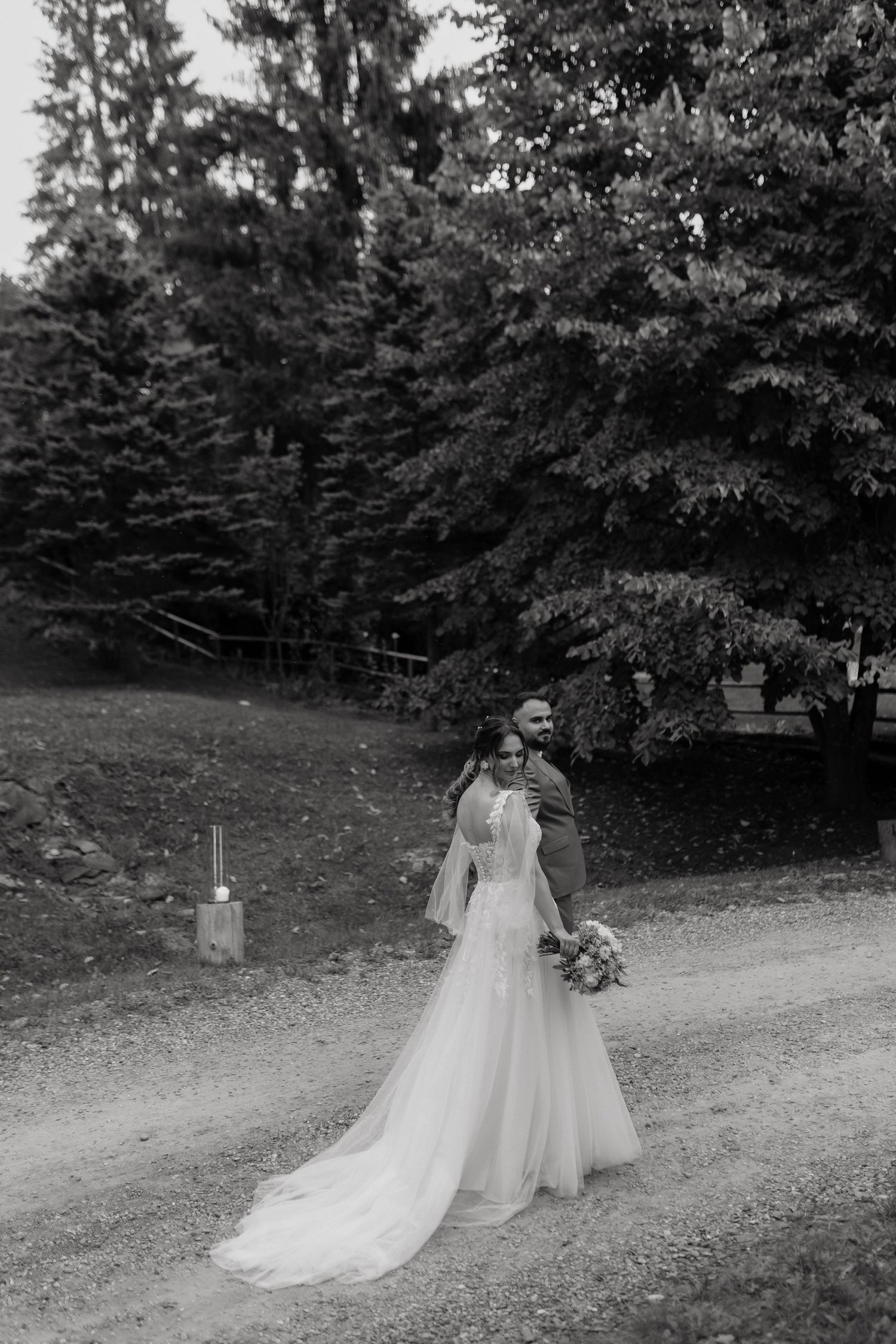 Two white wedding dresses displayed outdoors on dress forms against a wooded backdrop with lush greenery.