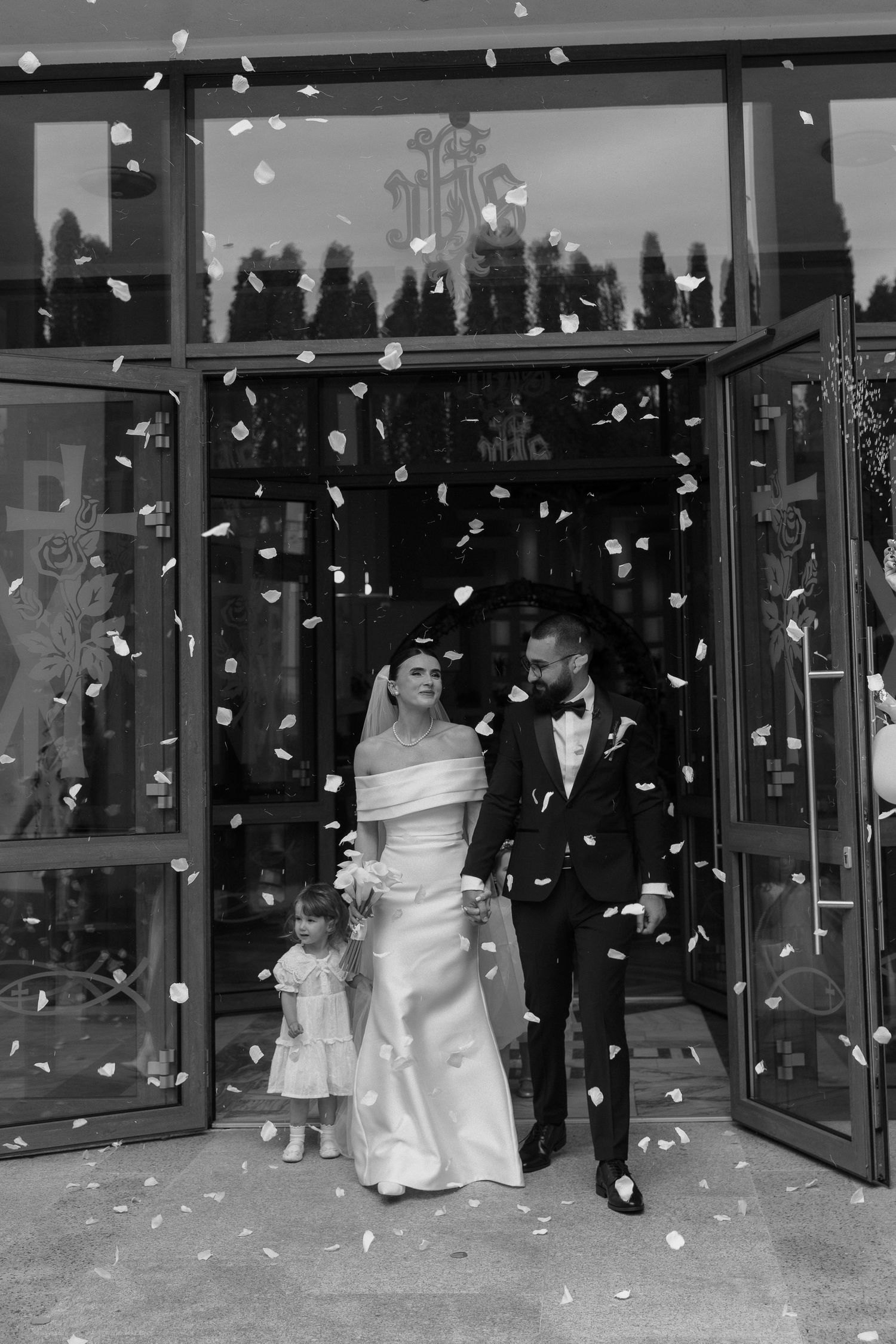 Wedding couple exits venue under a shower of white flower petals as guests celebrate their special moment.