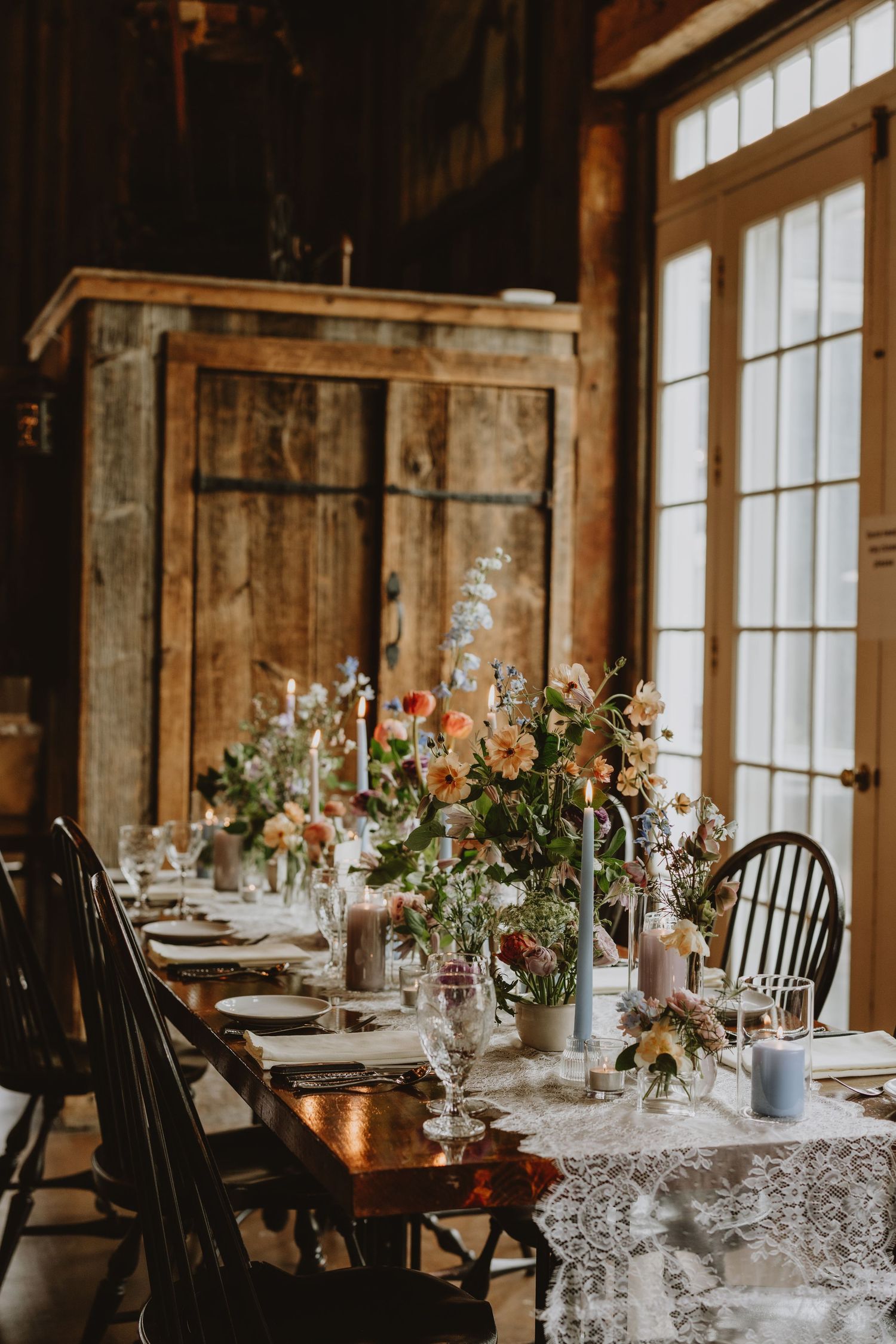 Rustic barn wedding reception table set with lace runner, colorful wildflower centerpieces, and candles.