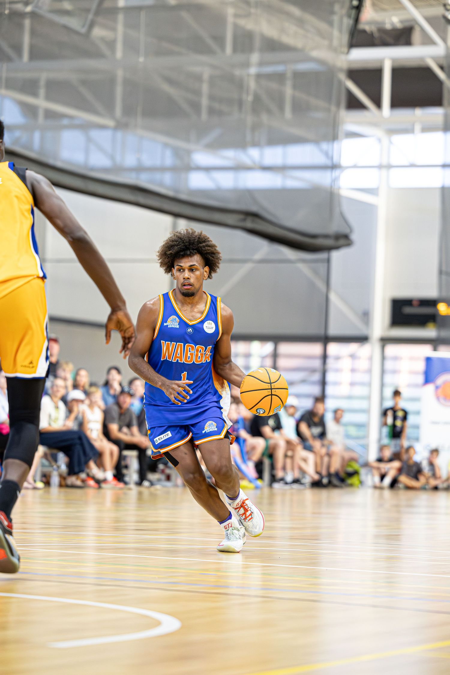 Basketball player in blue Nuggets jersey dribbles past defender on indoor court during competitive game.