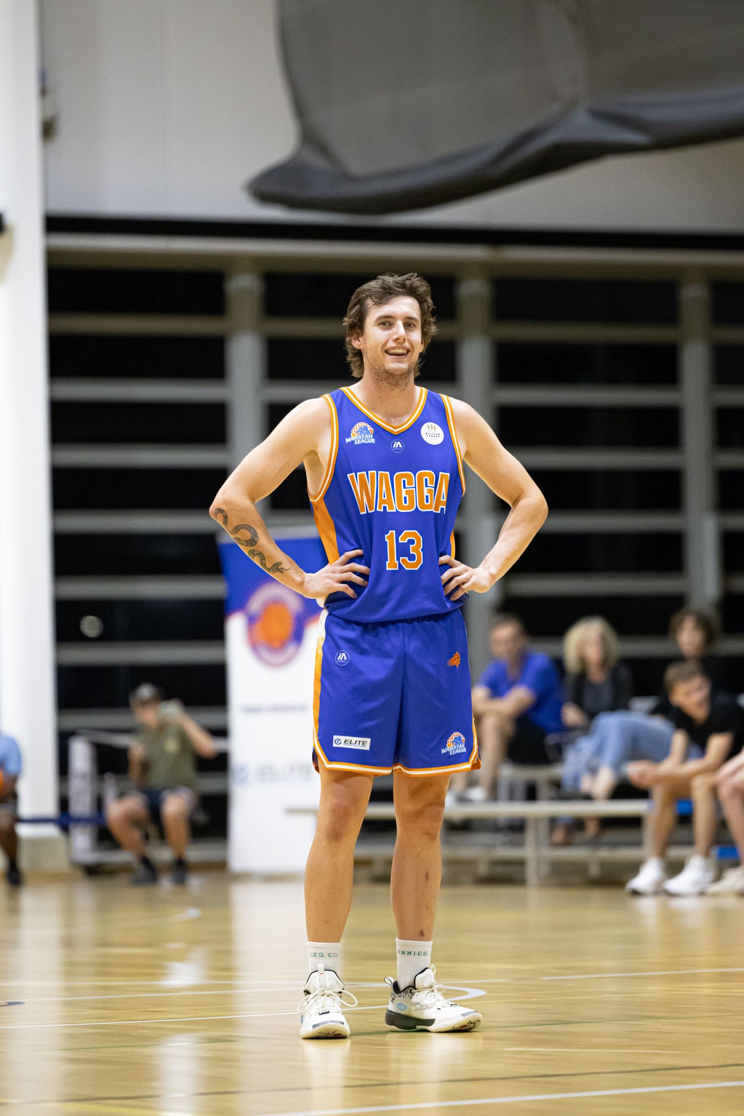 Basketball player wearing Wagga number 13 blue and gold uniform stands on indoor court with hands on hips.