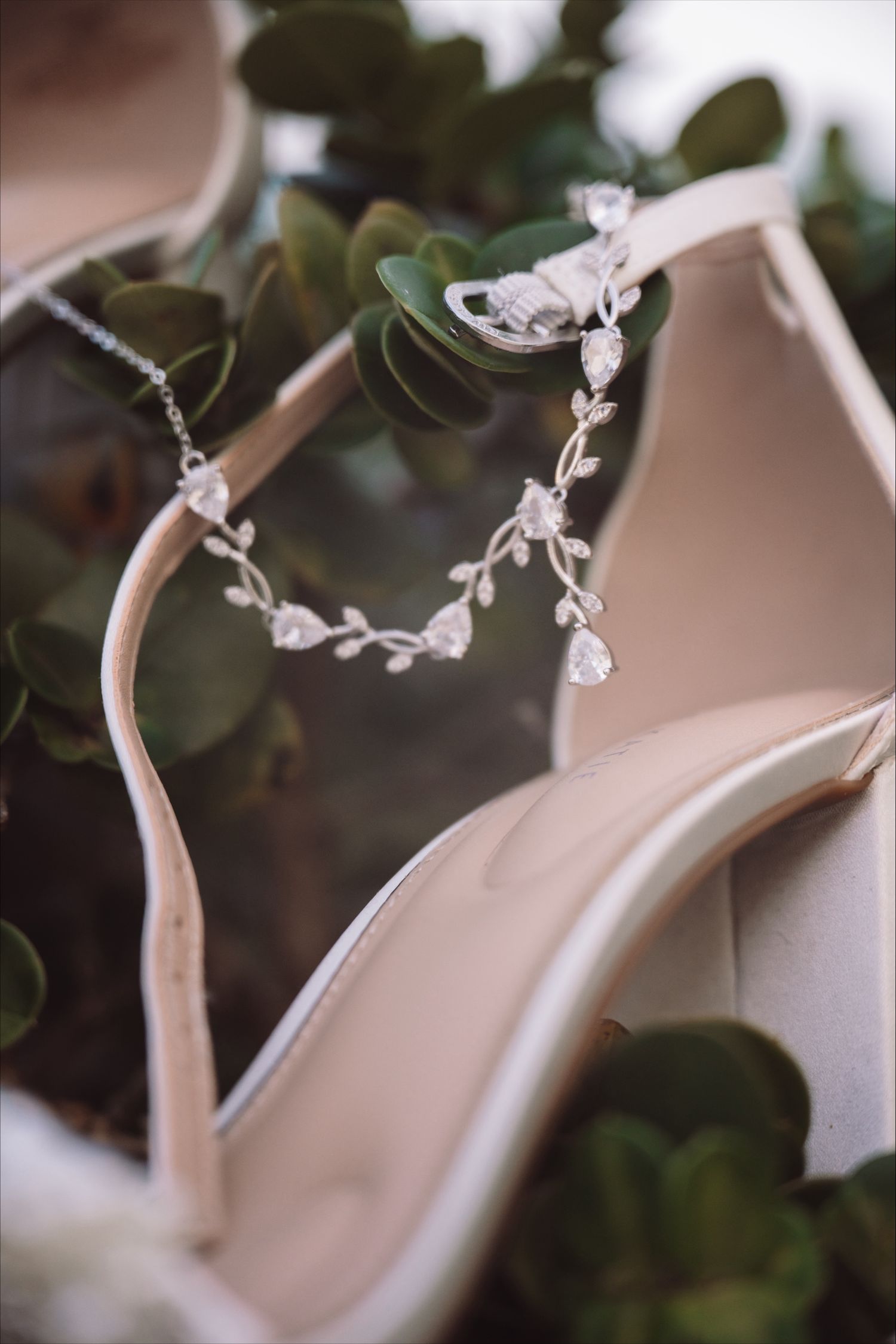 Delicate silver bridal jewelry with leaf motifs displayed against green foliage.
