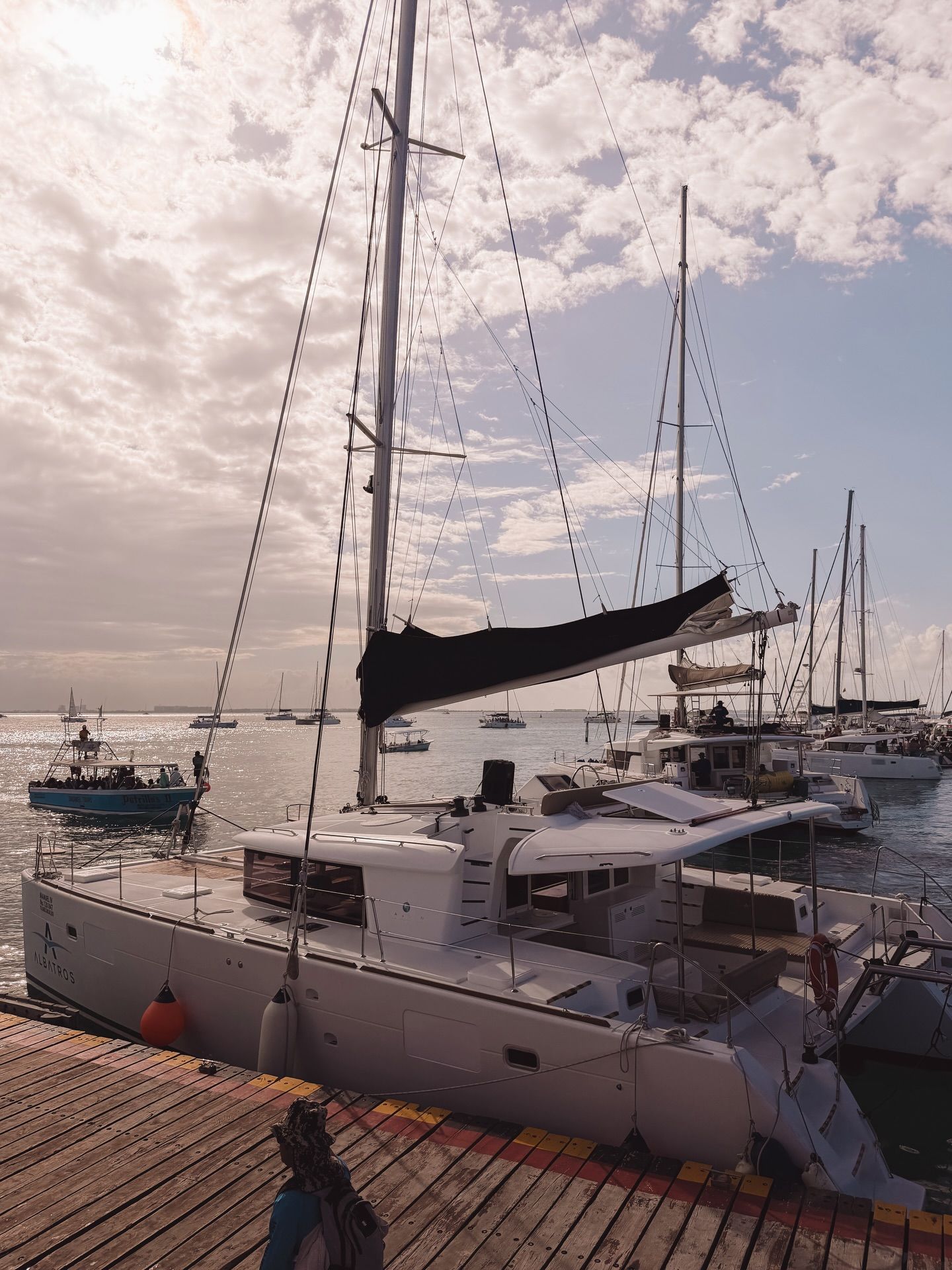 A series of sailboats and catamarans docked at a marina with cloudy skies overhead.