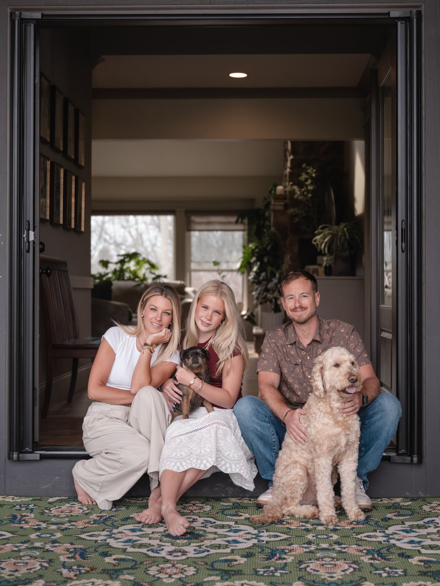 Family of two women and a man posing with two dogs in an open doorway of a stylish home.