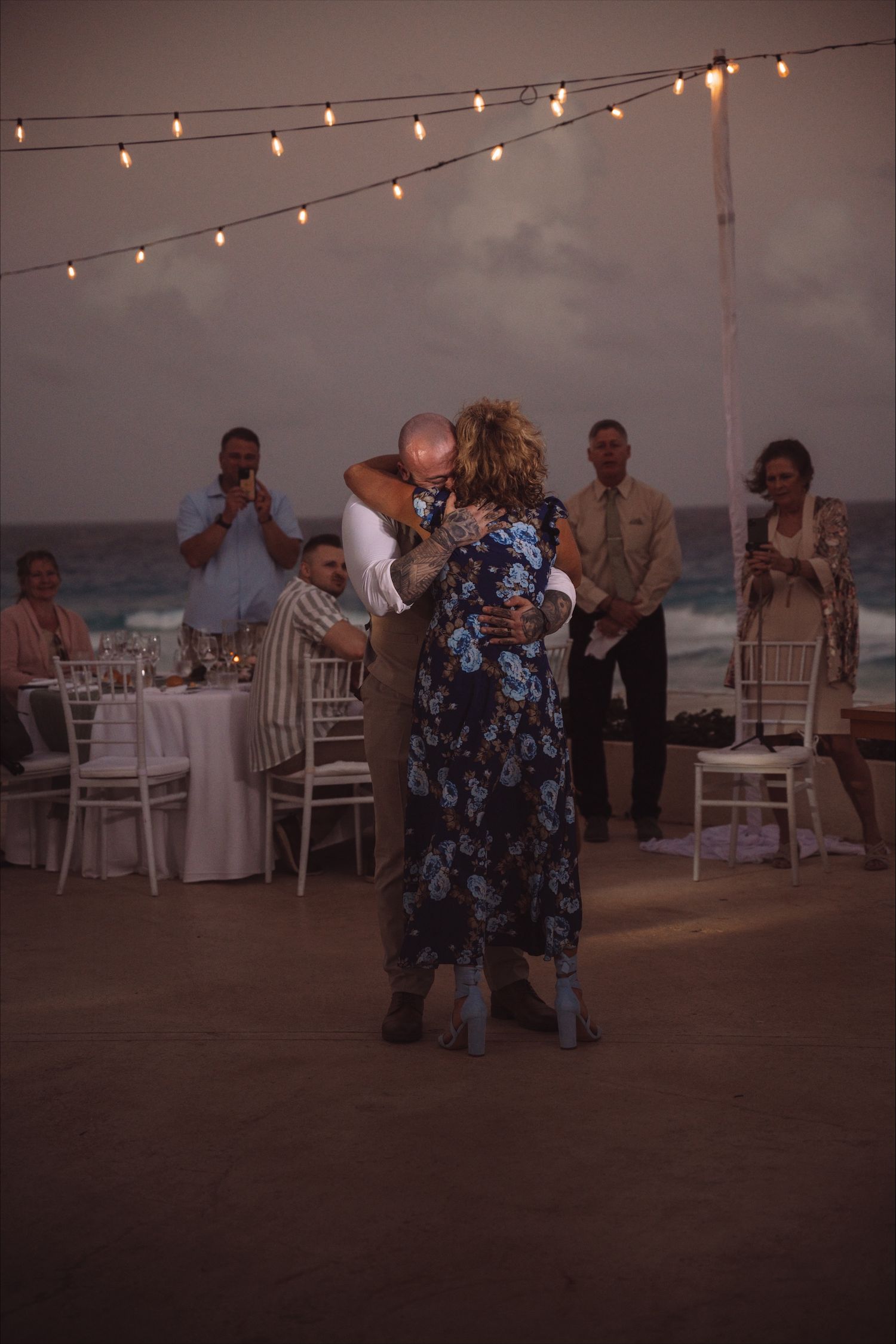 Wedding guests dancing under string lights at an outdoor beach reception.