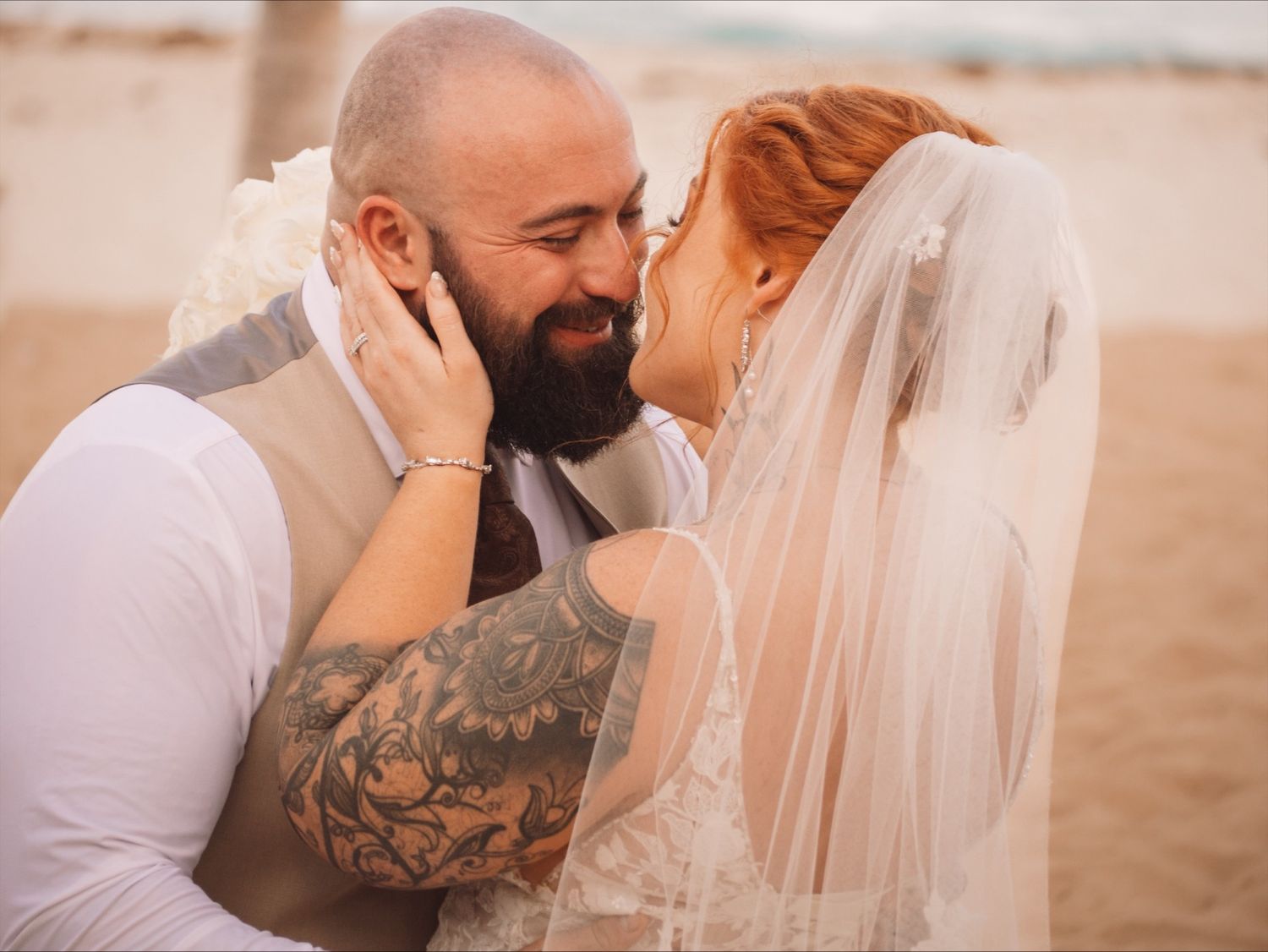 A tender wedding moment captured on a beach with soft lighting.