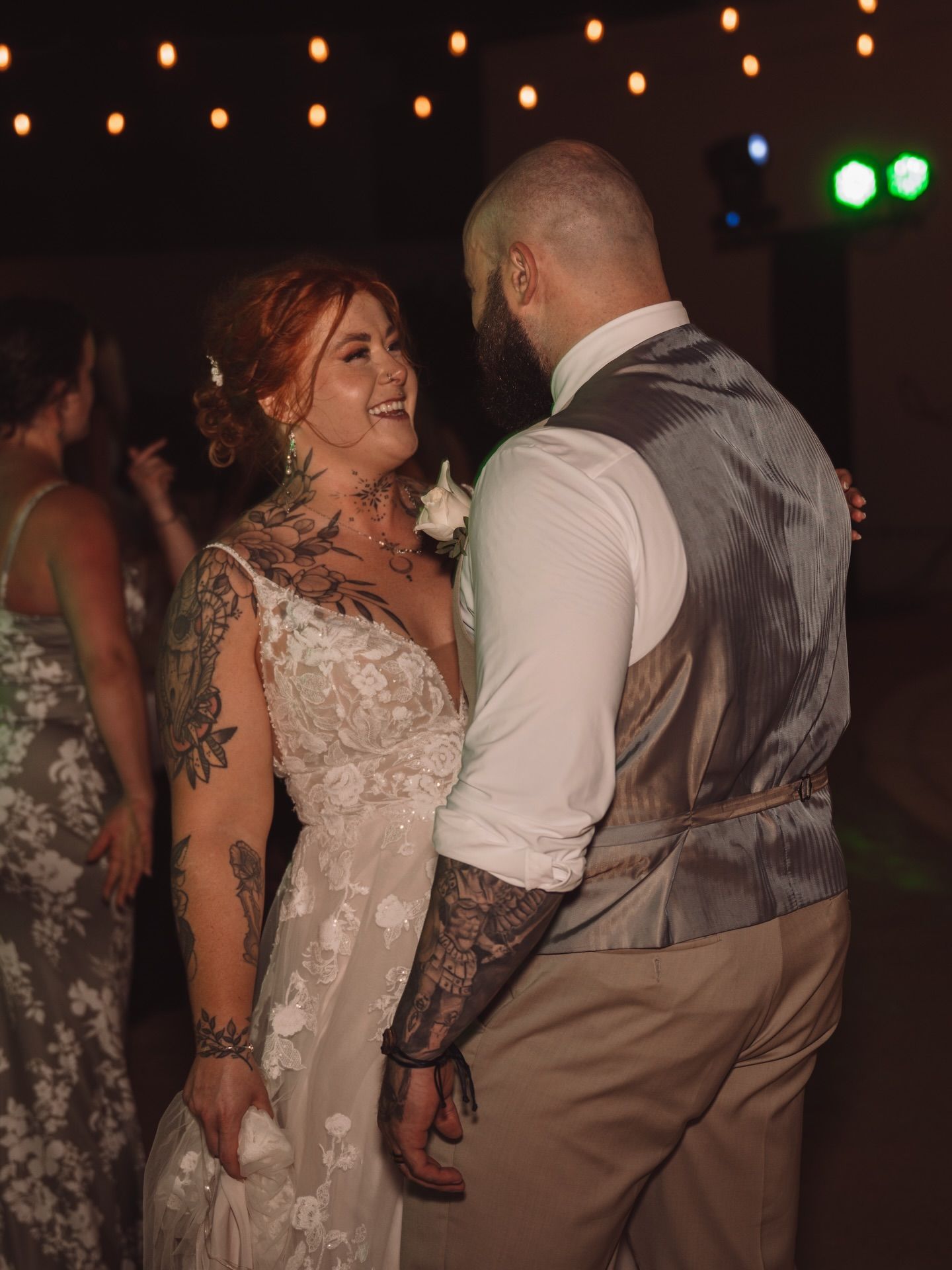 A bride and groom share an intimate dance moment on the reception floor with string lights glowing overhead.