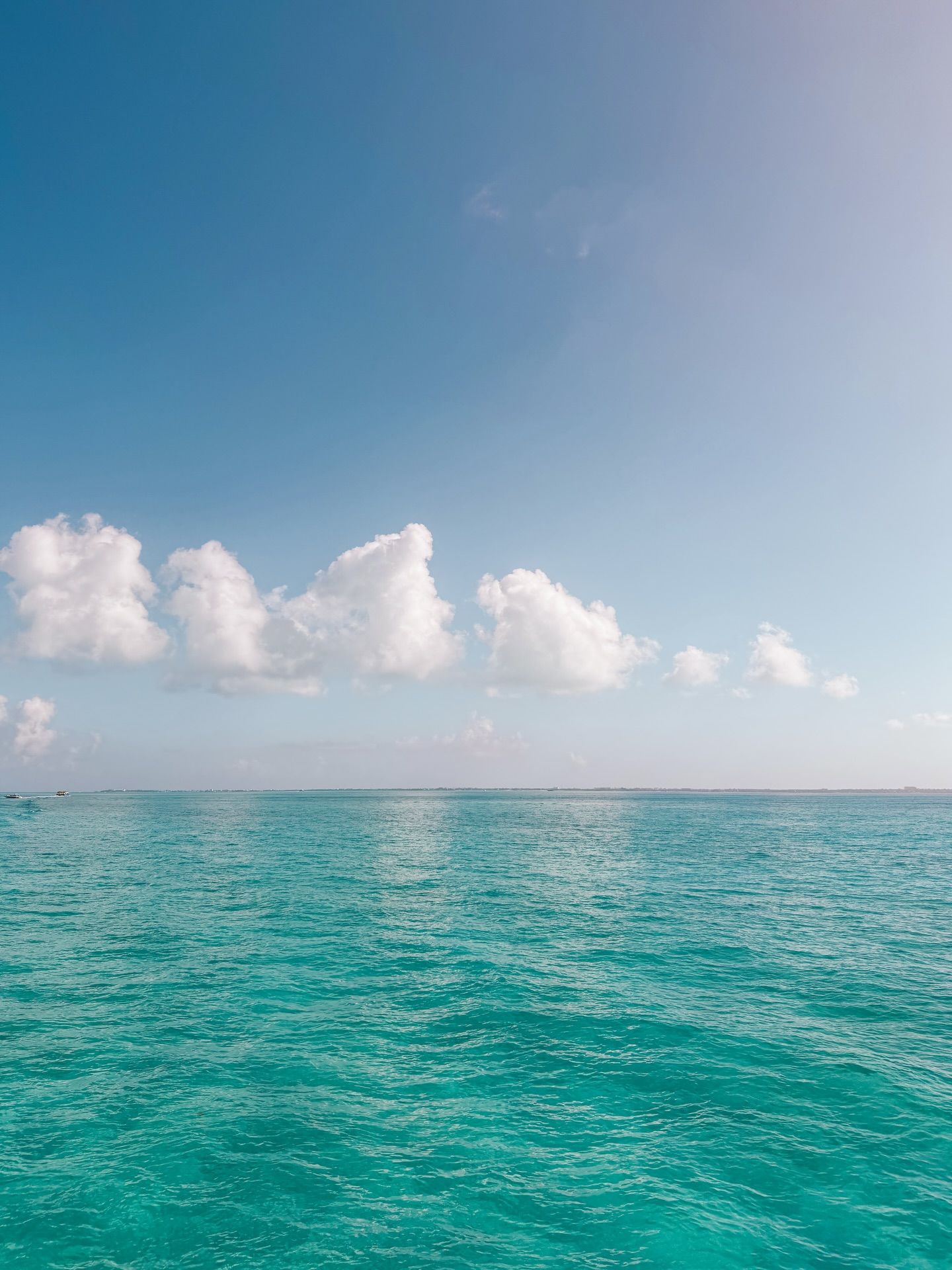Turquoise ocean waters meet fluffy white clouds in a serene seascape under bright blue Caribbean skies.