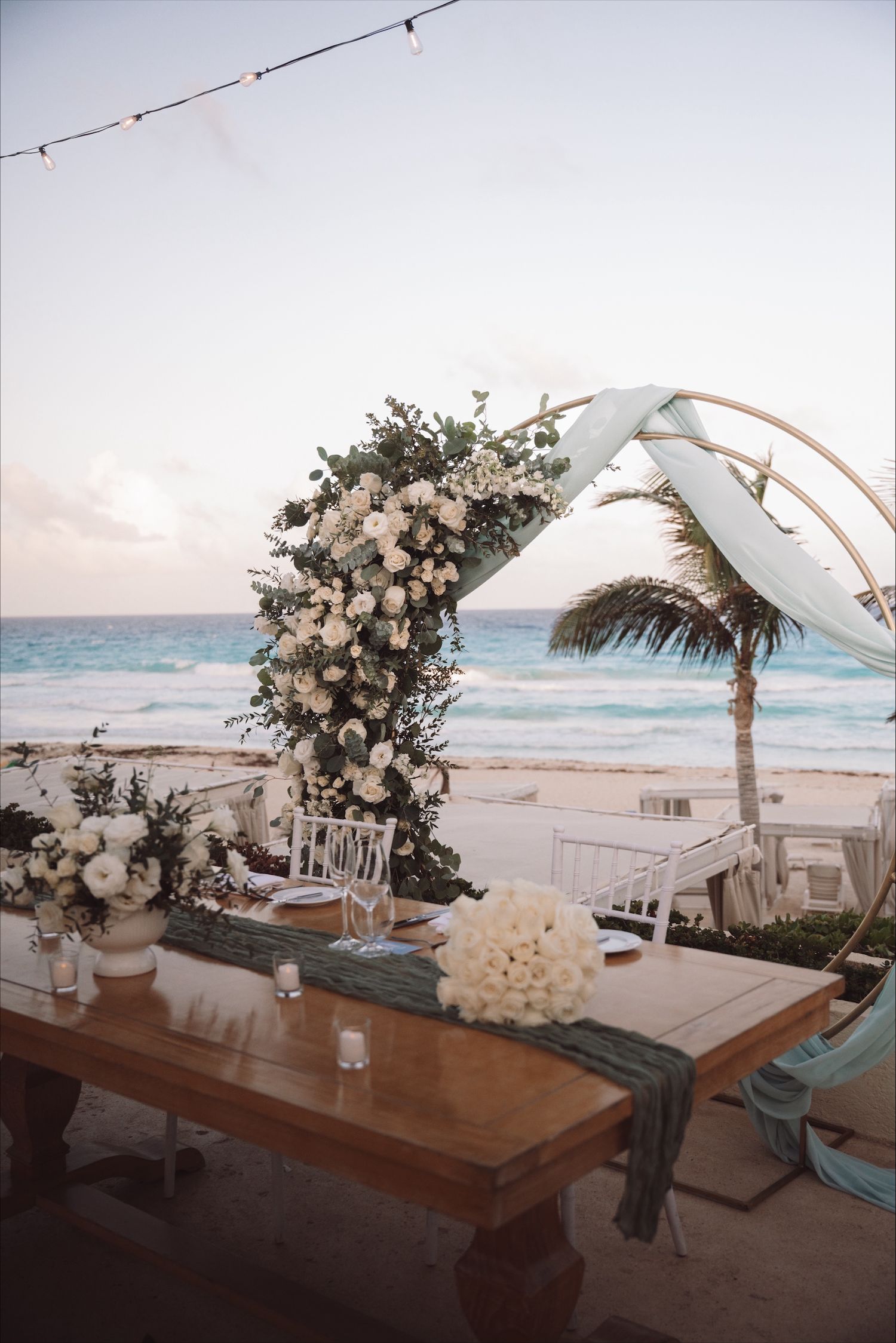 Beach wedding ceremony setup with white arch, flowers and wooden benches overlooking the ocean.