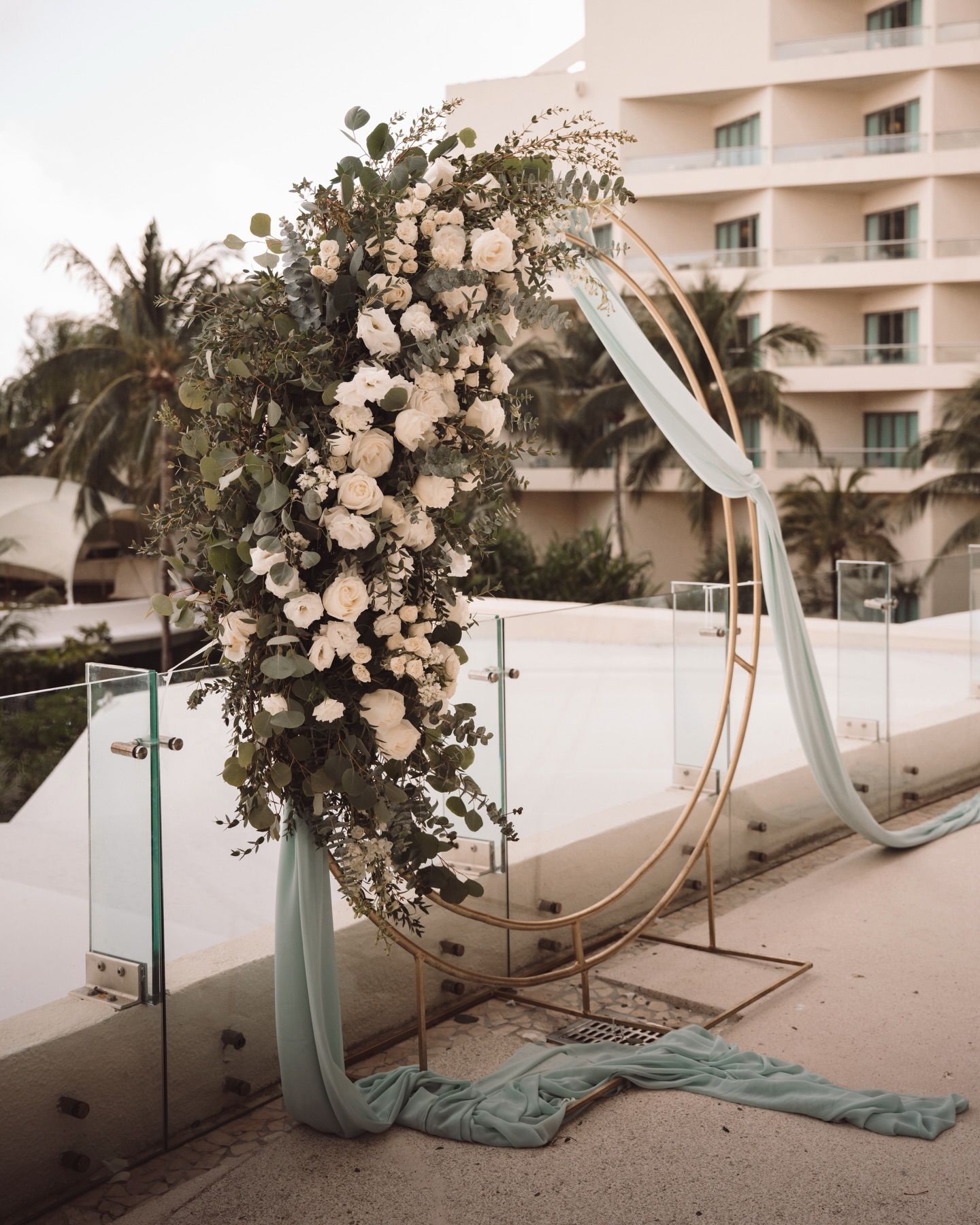 Wedding arch installation sequence showing floral arrangements and fabric being set up on a beachfront venue.
