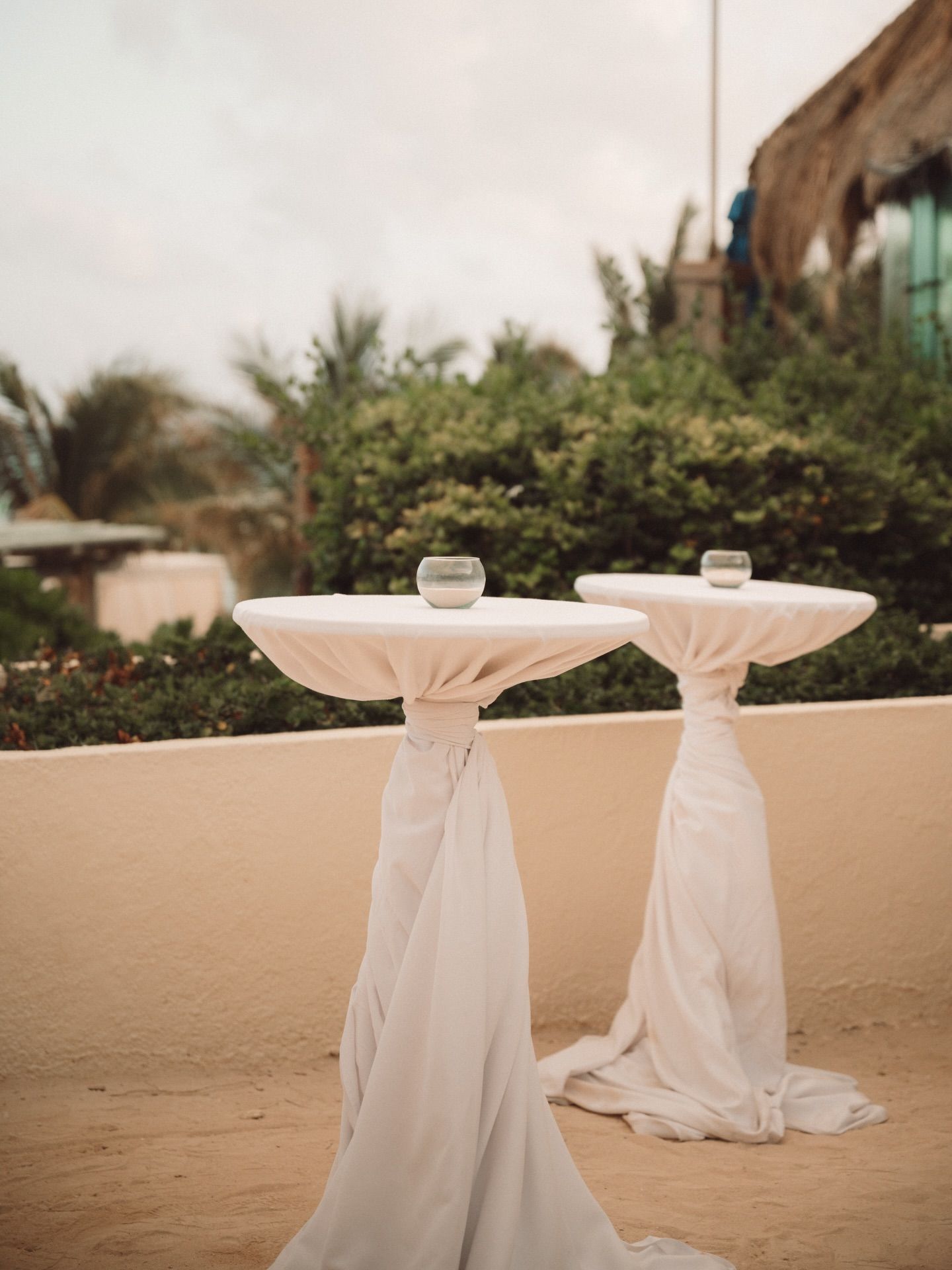 White draped cocktail tables set up on a sandy beach for an outdoor event.