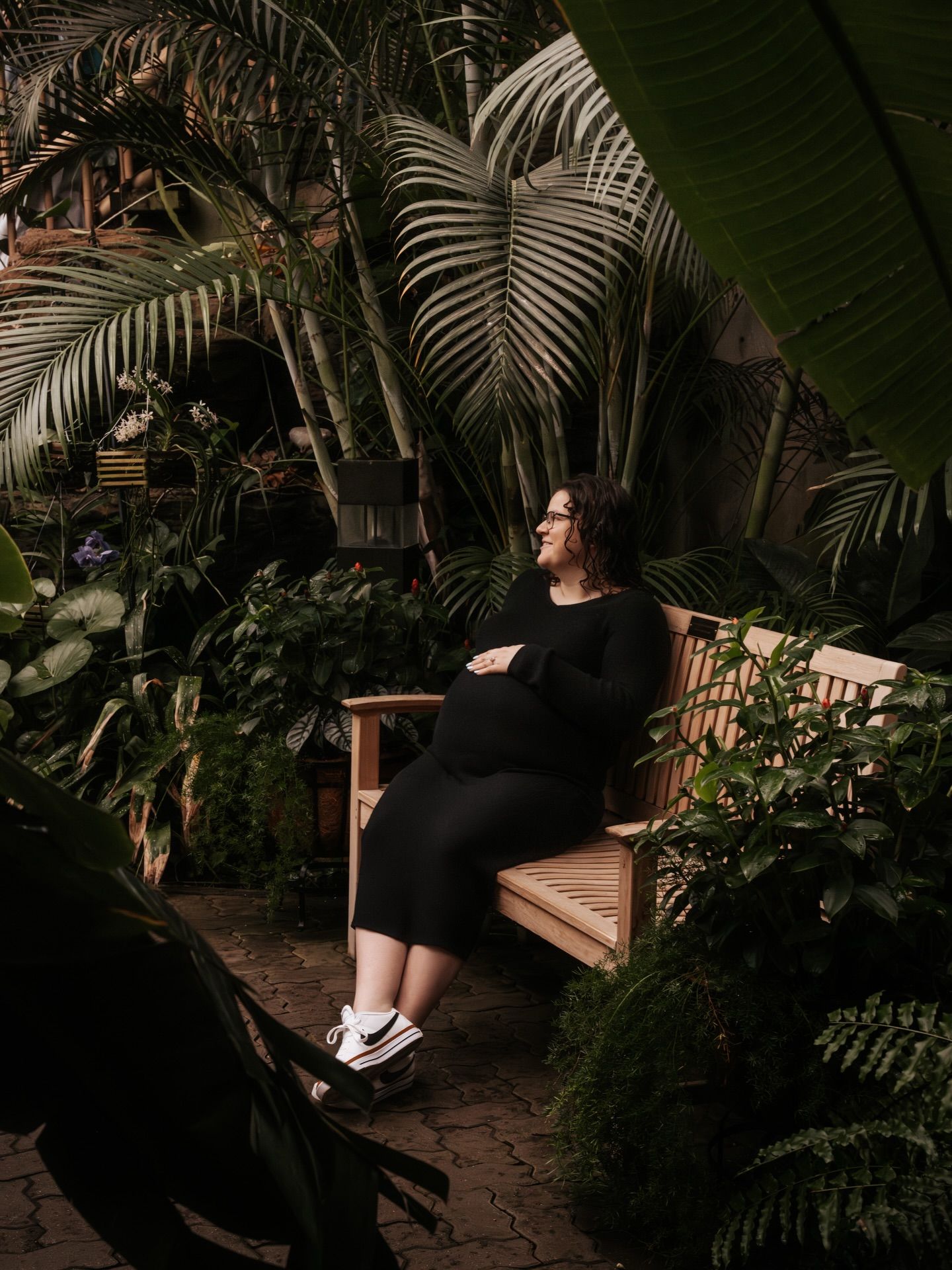 A peaceful garden scene with someone relaxing on a wooden bench surrounded by tropical plants.