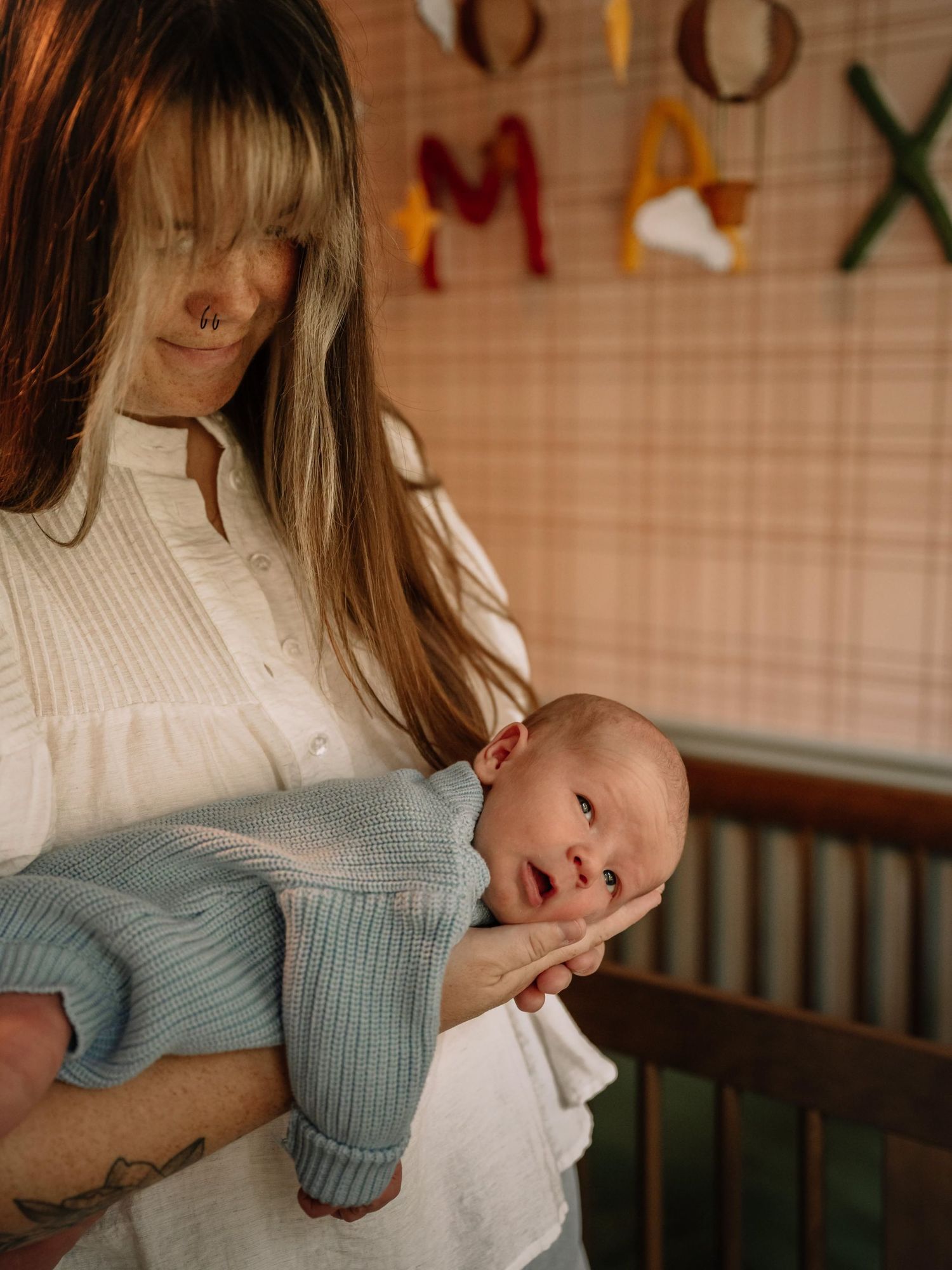 A mother in a white blouse tenderly holds her newborn baby in a cozy nursery room.