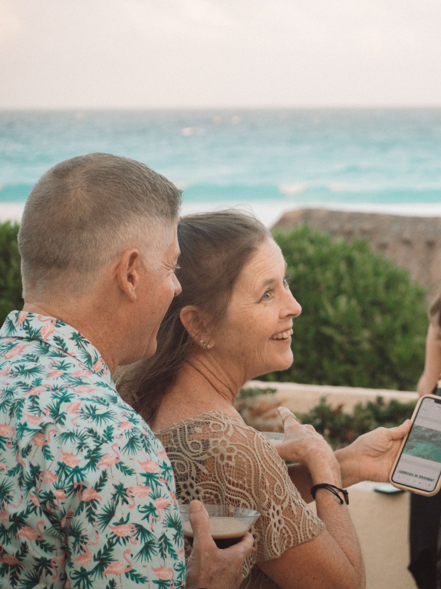 A couple sits together outdoors enjoying a scenic view of turquoise waters and lush greenery on a sunny day.