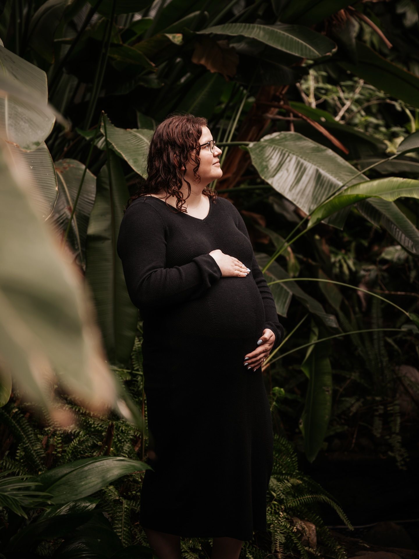 Couple sharing an intimate moment among tropical foliage in dark, romantic lighting.