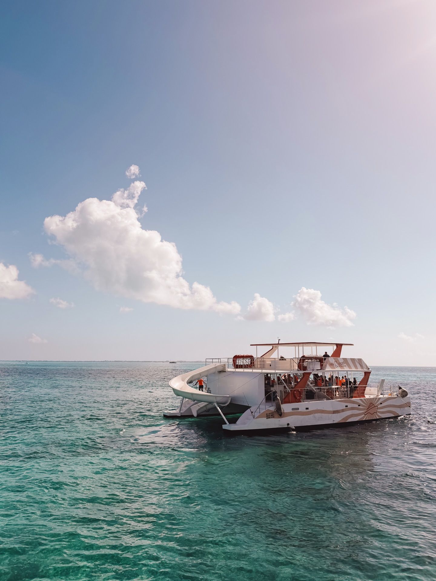 A white catamaran boat cruises on turquoise Caribbean waters under puffy white clouds and blue skies.