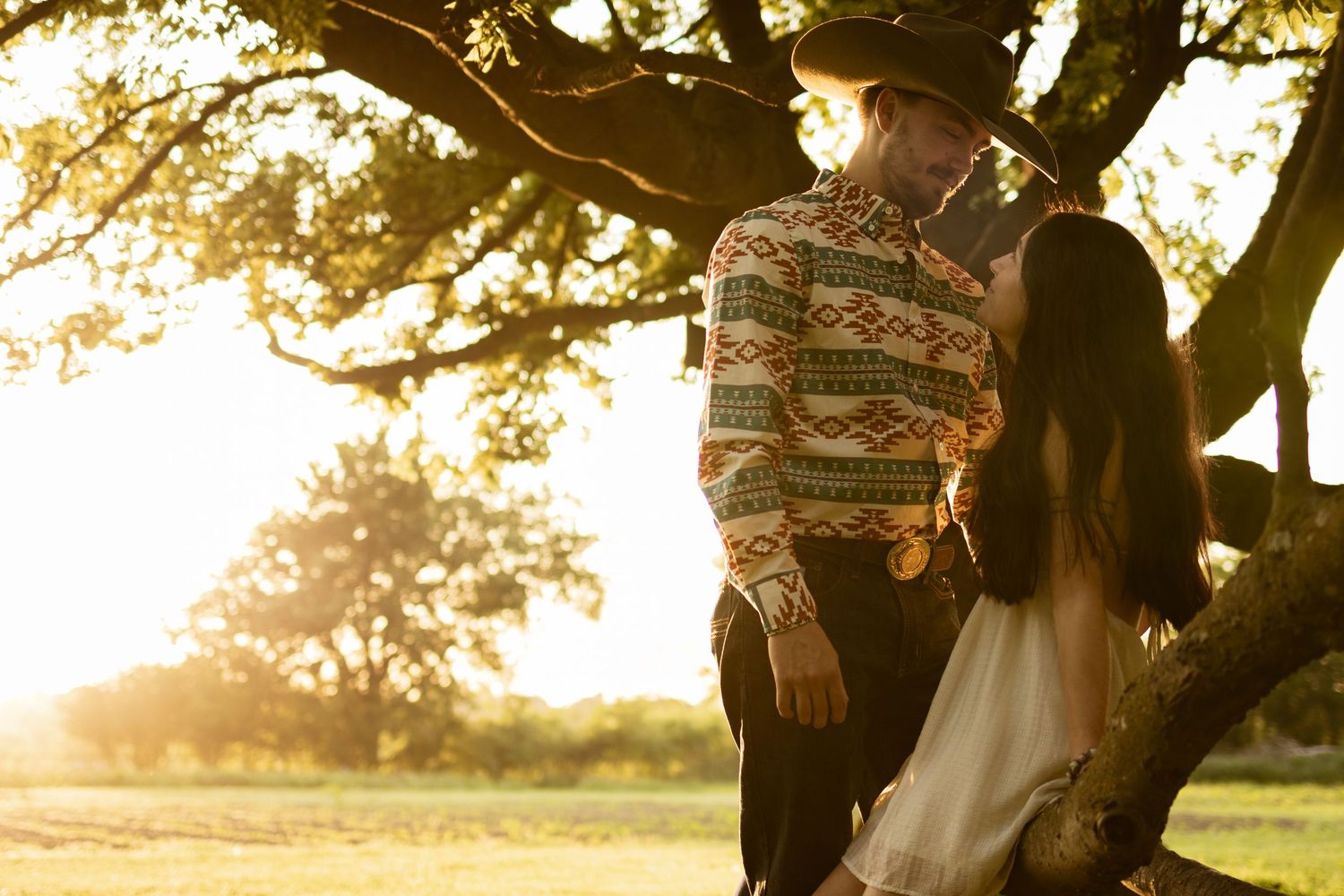 Couple sharing a romantic moment under a golden sunset tree in a lush green park setting.