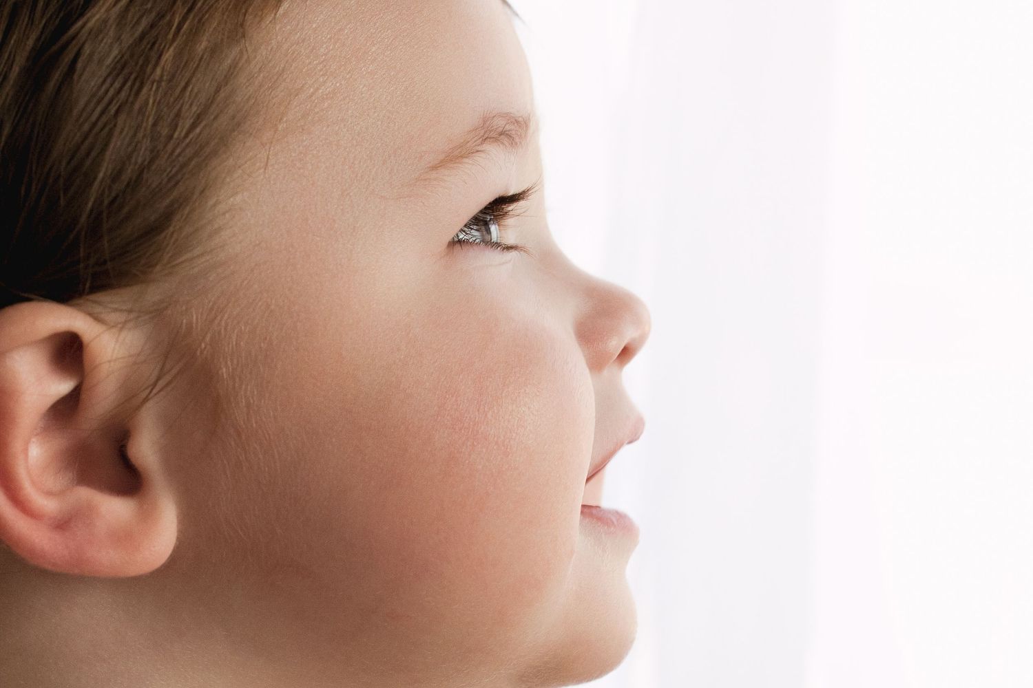 Close-up profile of a young child looking upward with soft natural lighting highlighting their delicate features.
