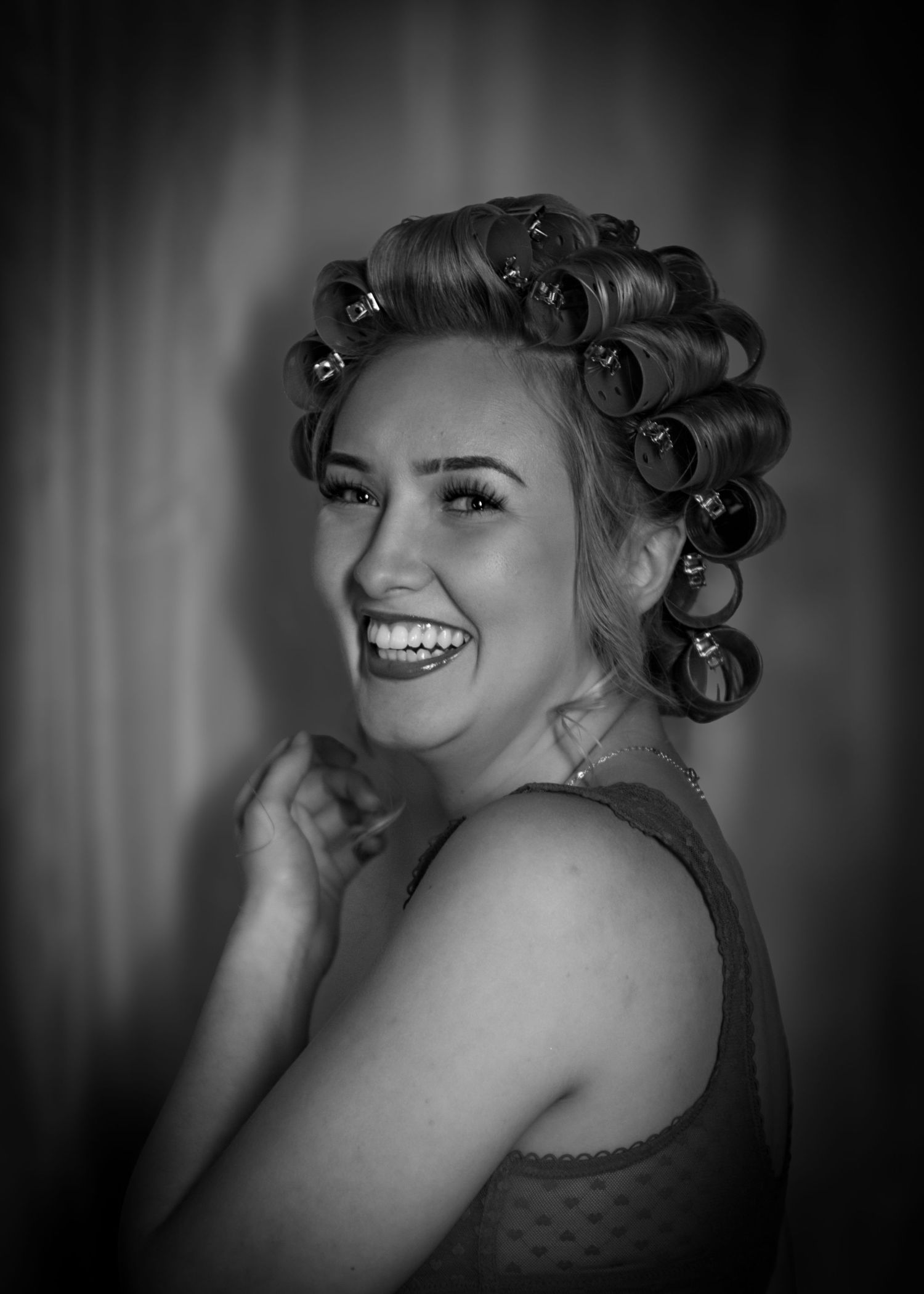 Laughing woman with hair rollers smiling in black and white portrait photo.