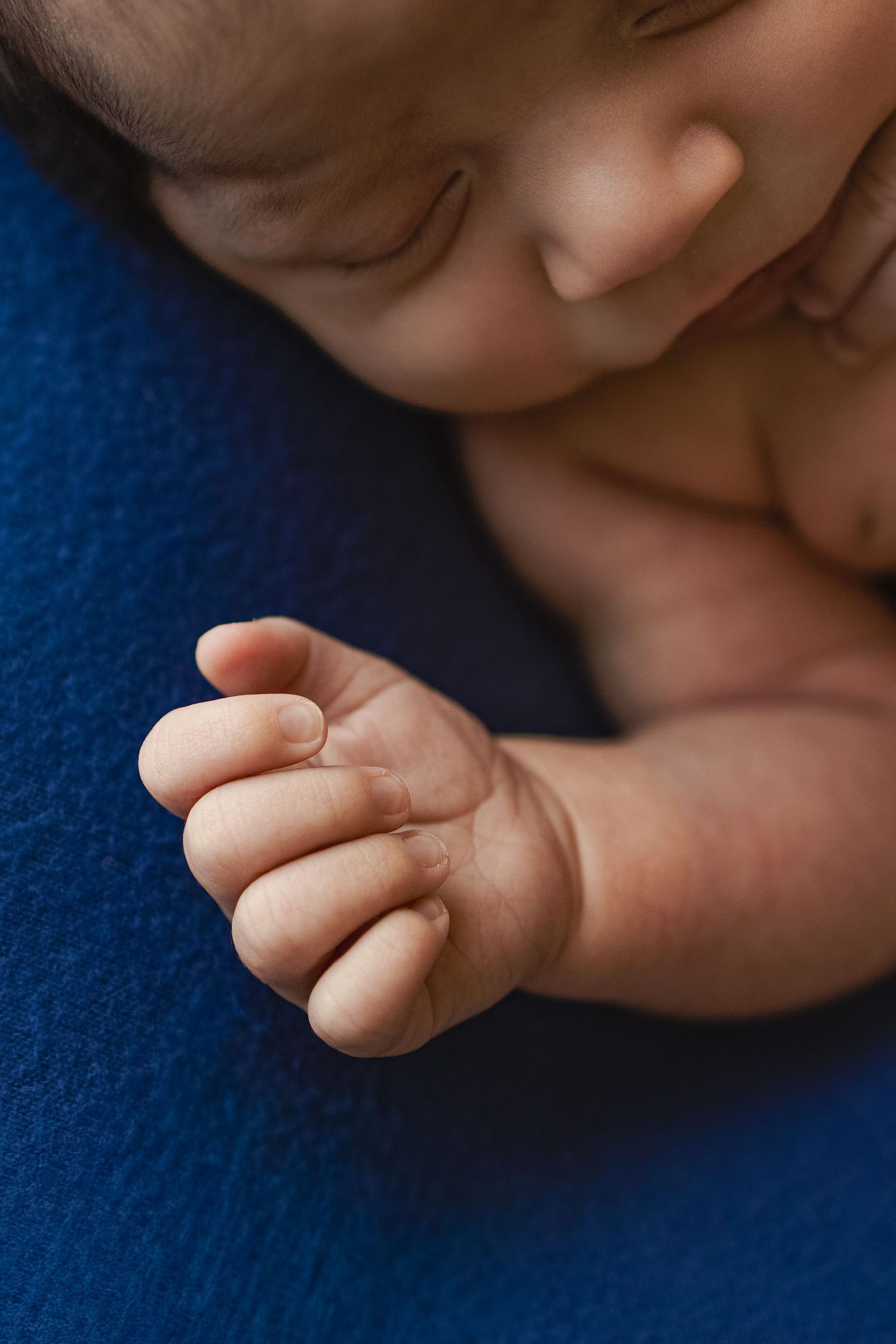 Close-up of a sleeping newborn baby's tiny clenched fist resting on a blue blanket.