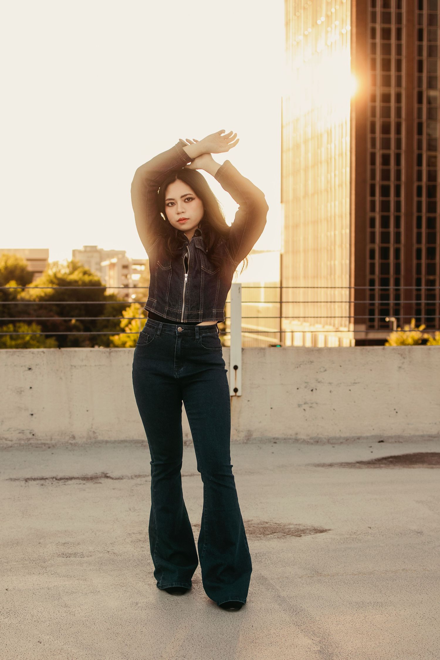 Woman in flare jeans poses on rooftop at golden hour sunset.