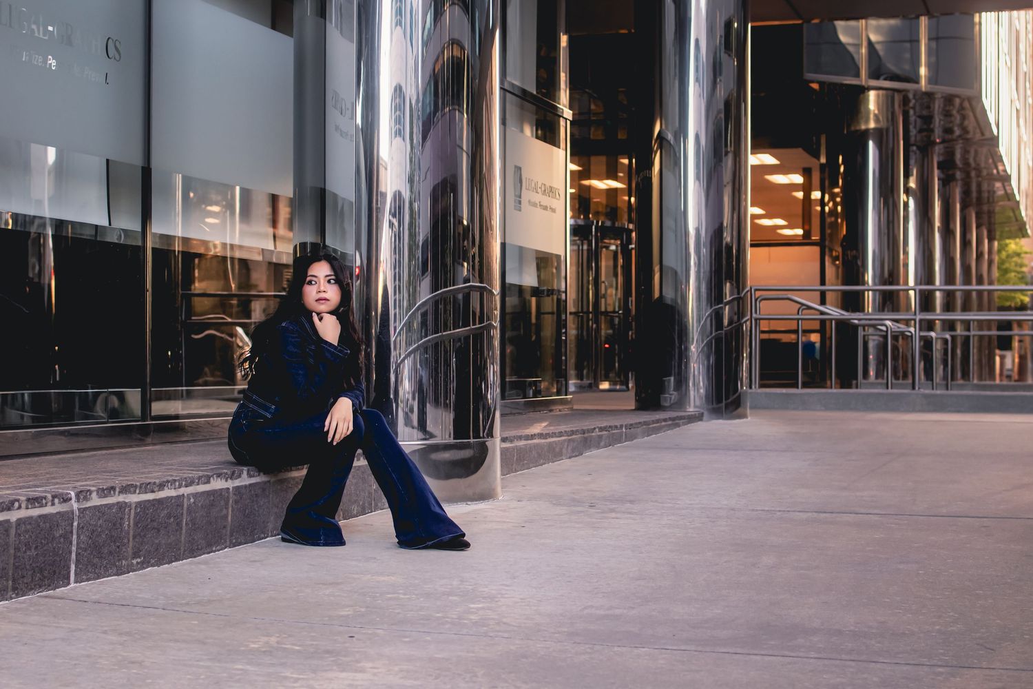 Woman in navy blue wide-leg pants sitting outside modern glass building facade.