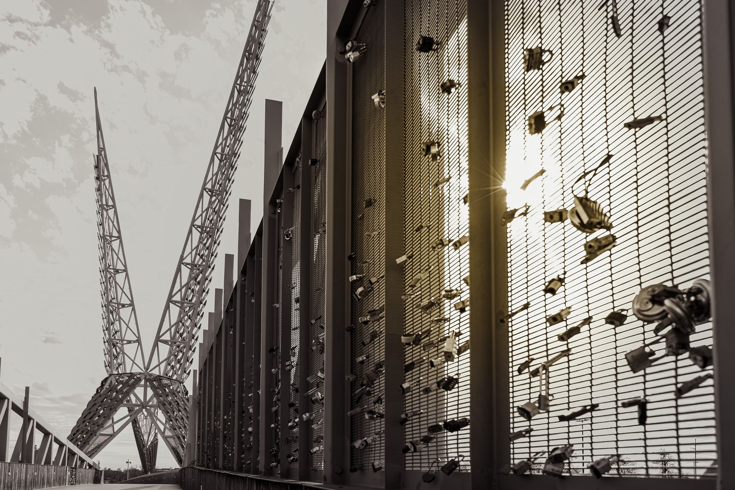 Modern bridge walkway with decorative metal mesh wall adorned with padlocks glowing in warm sunlight.