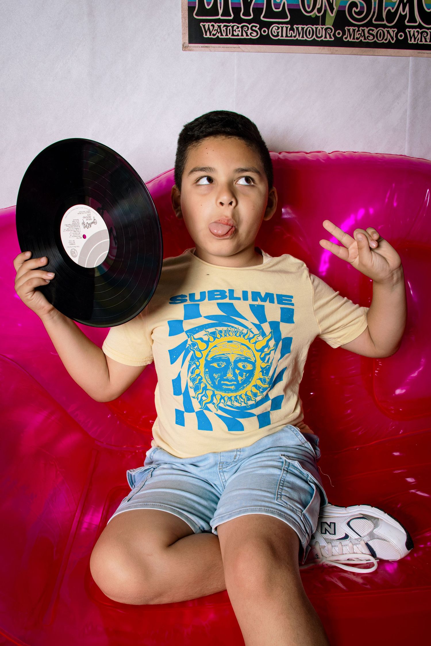 Boy in Sublime t-shirt holds vinyl record on pink inflatable sofa making a funny face.
