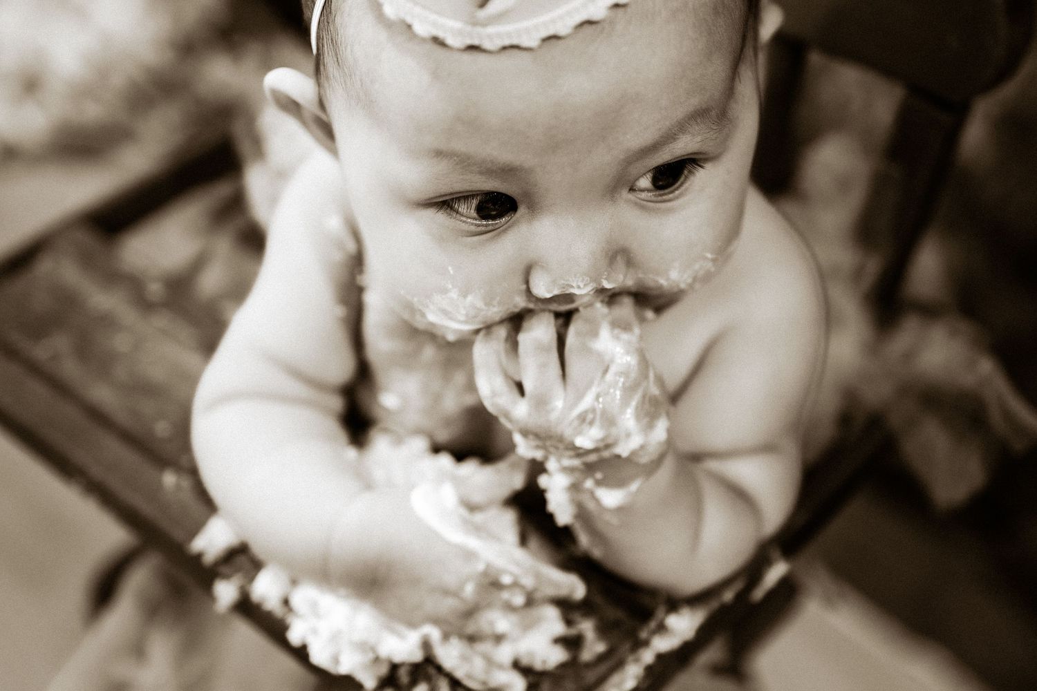 Sepia-toned photo of a baby girl eating smash cake with her hands during a first birthday photo session.