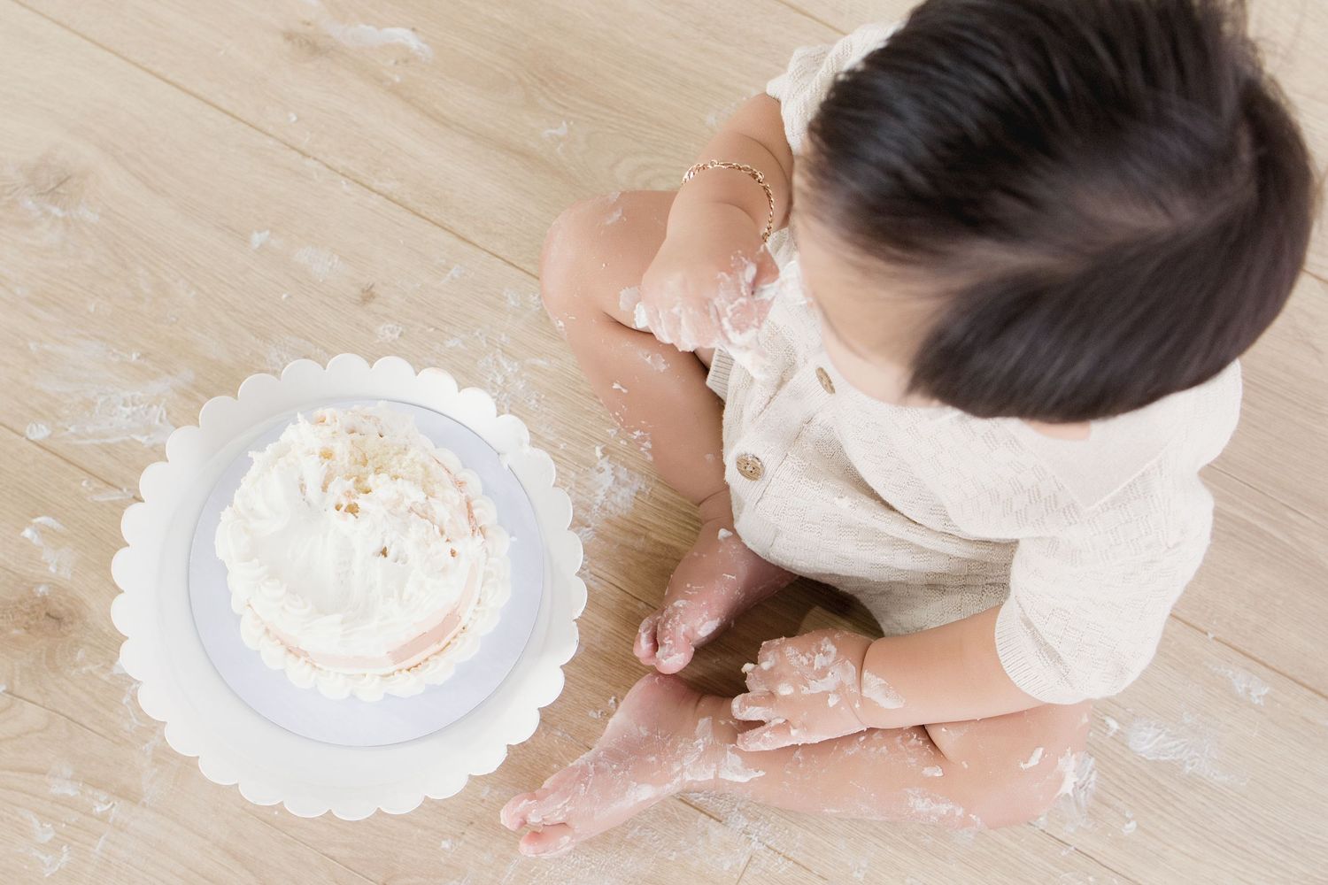 Baby smashing a white frosted cake on a wooden floor during a first birthday cake smash photo session.