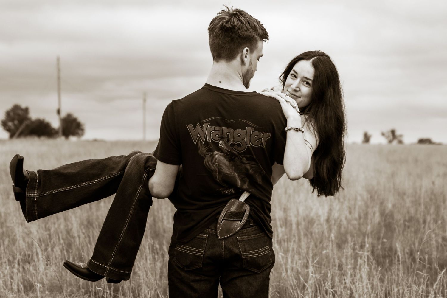Man carrying woman in his arms in a romantic sepia-toned outdoor field photo.