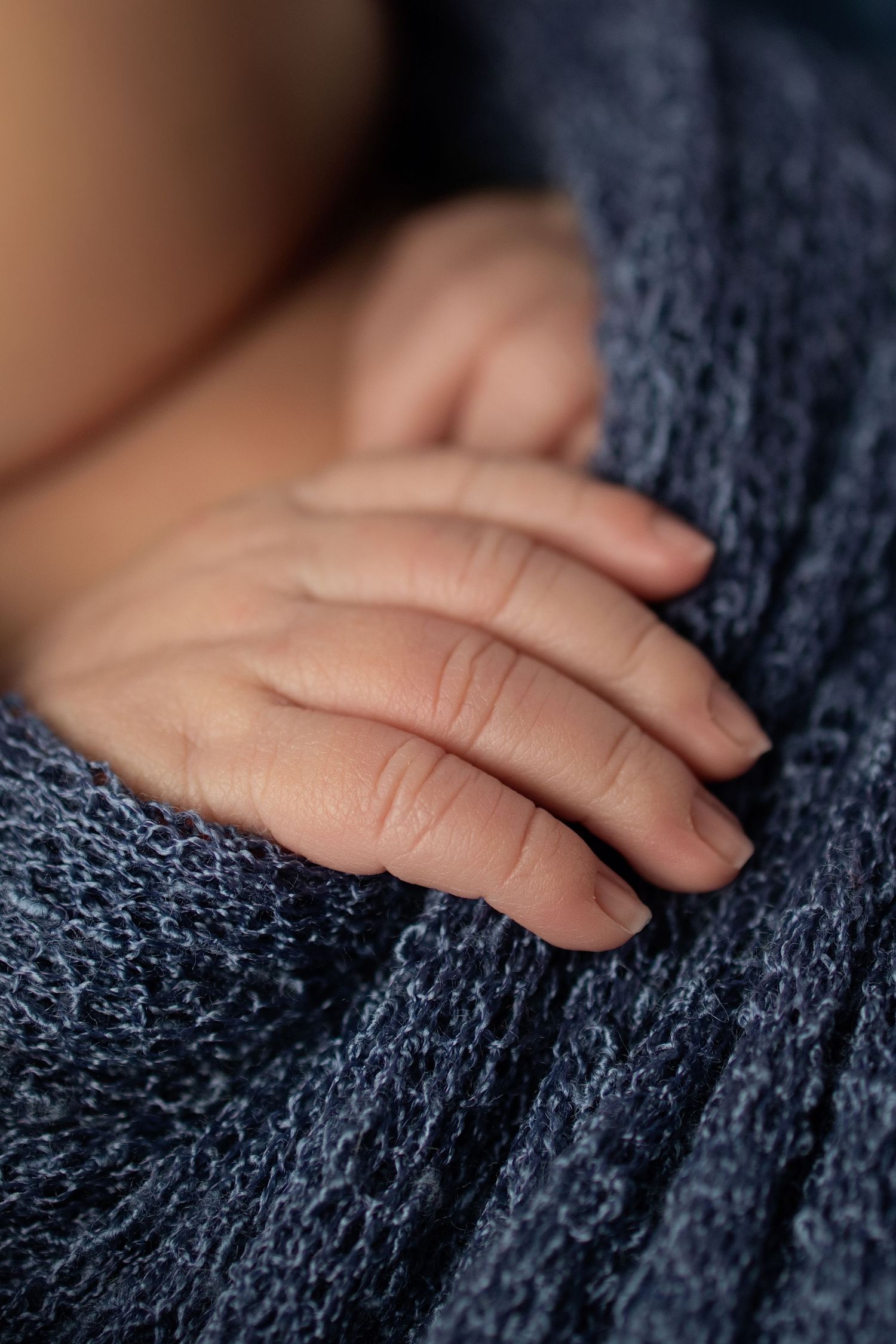 Close-up of a newborn baby's tiny hand resting on a soft blue knit blanket.