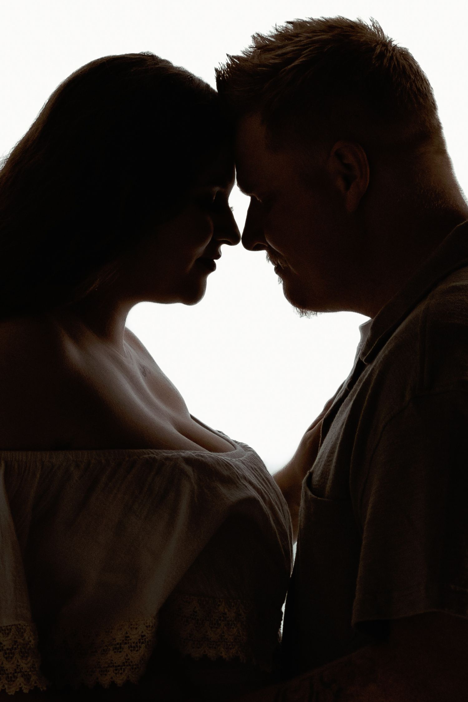 Romantic backlit silhouette portrait of couple in intimate pose against light background.