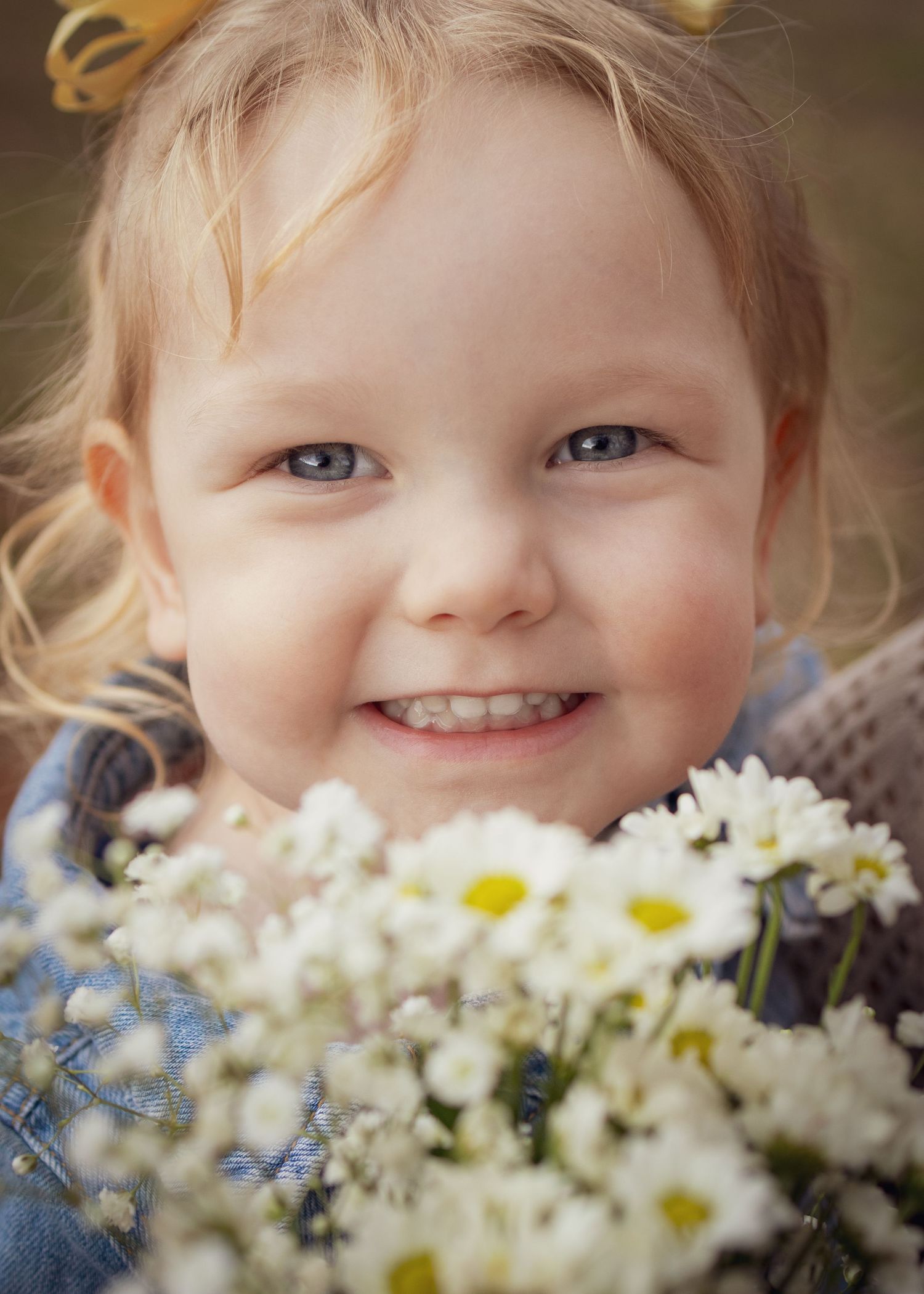 Smiling toddler girl with blue eyes holding a bouquet of white daisies outdoors.