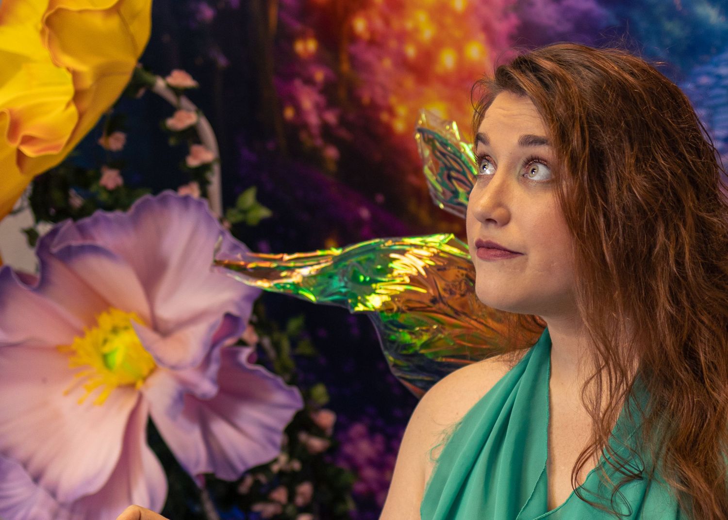 Woman with auburn hair poses with a colorful dragon on her shoulder against a vibrant fantasy floral background.
