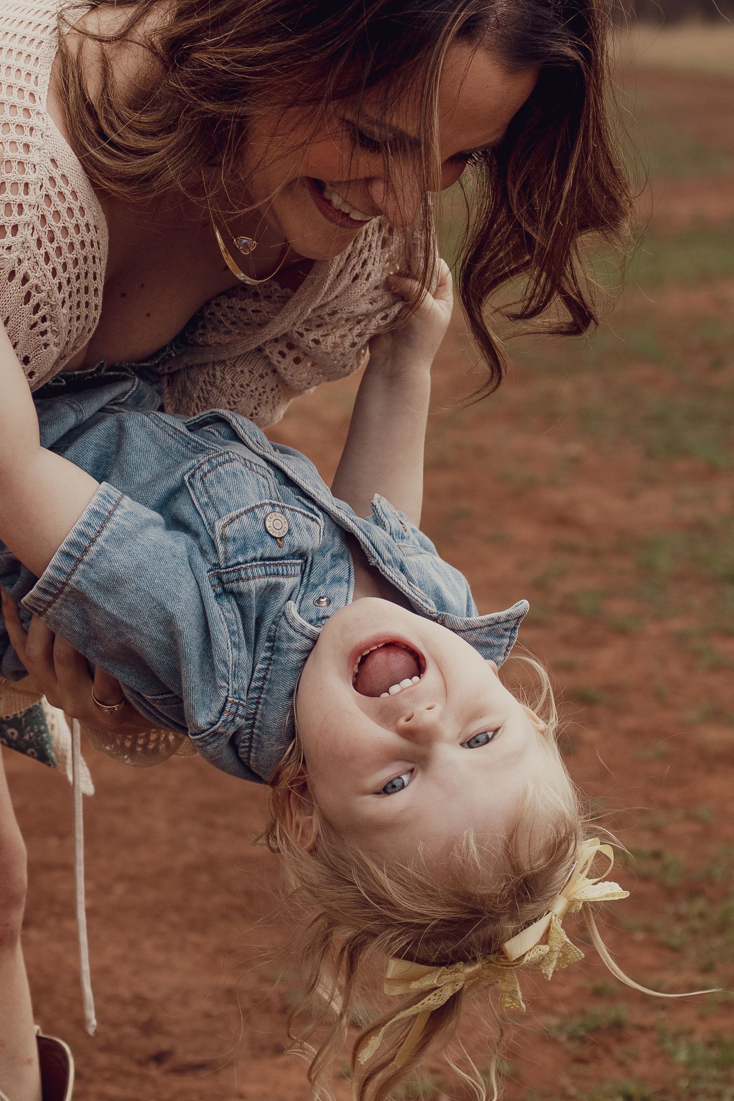 A joyful mother swings her laughing toddler upside down outdoors, both sharing a playful moment of happiness.
