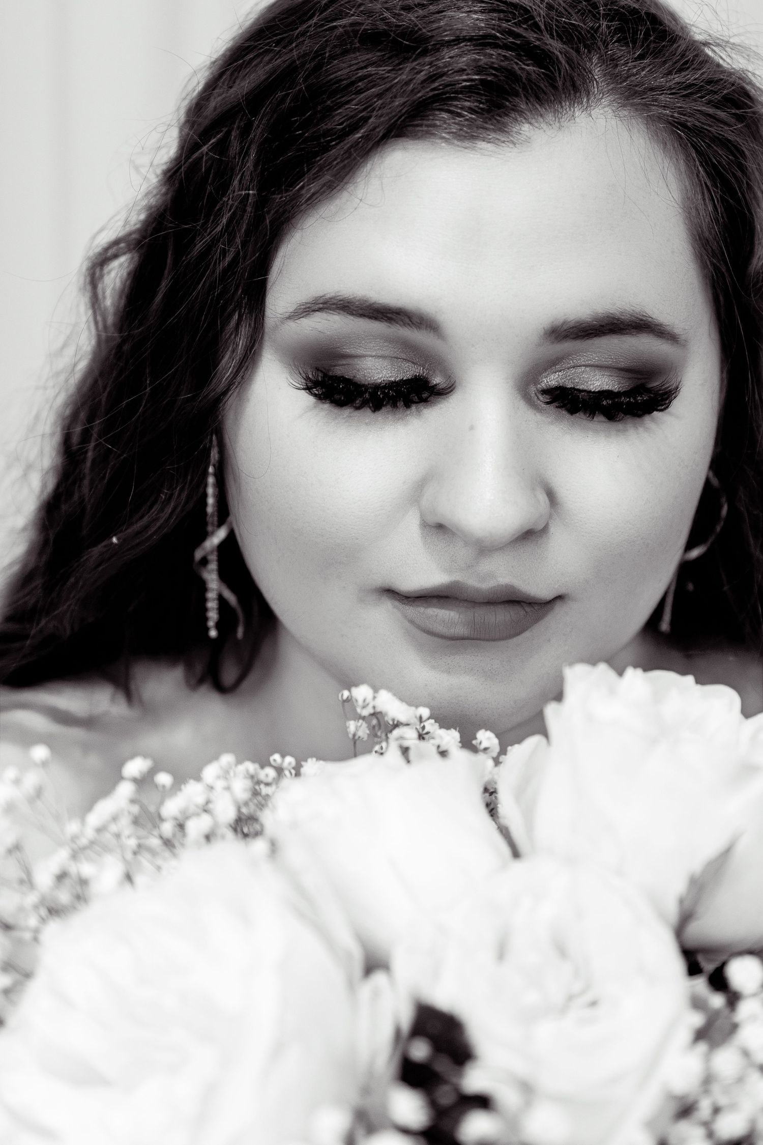 Black and white portrait of a bride with dramatic eye makeup holding a bouquet of white roses and baby's breath.