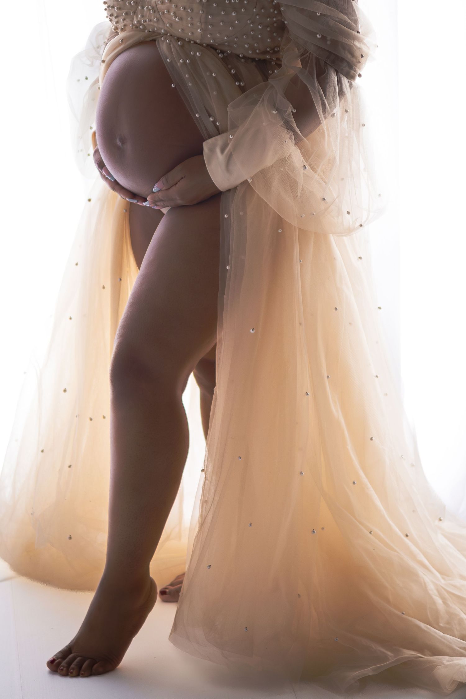 Artistic silhouette maternity photo showing pregnant belly with flowing tulle dress and sparkles.