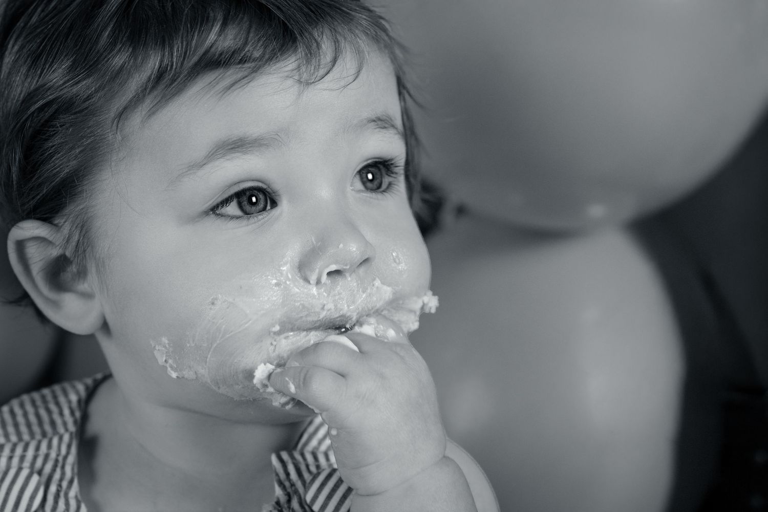 Black and white close-up of a baby with cake frosting on face, enjoying their first birthday treat.