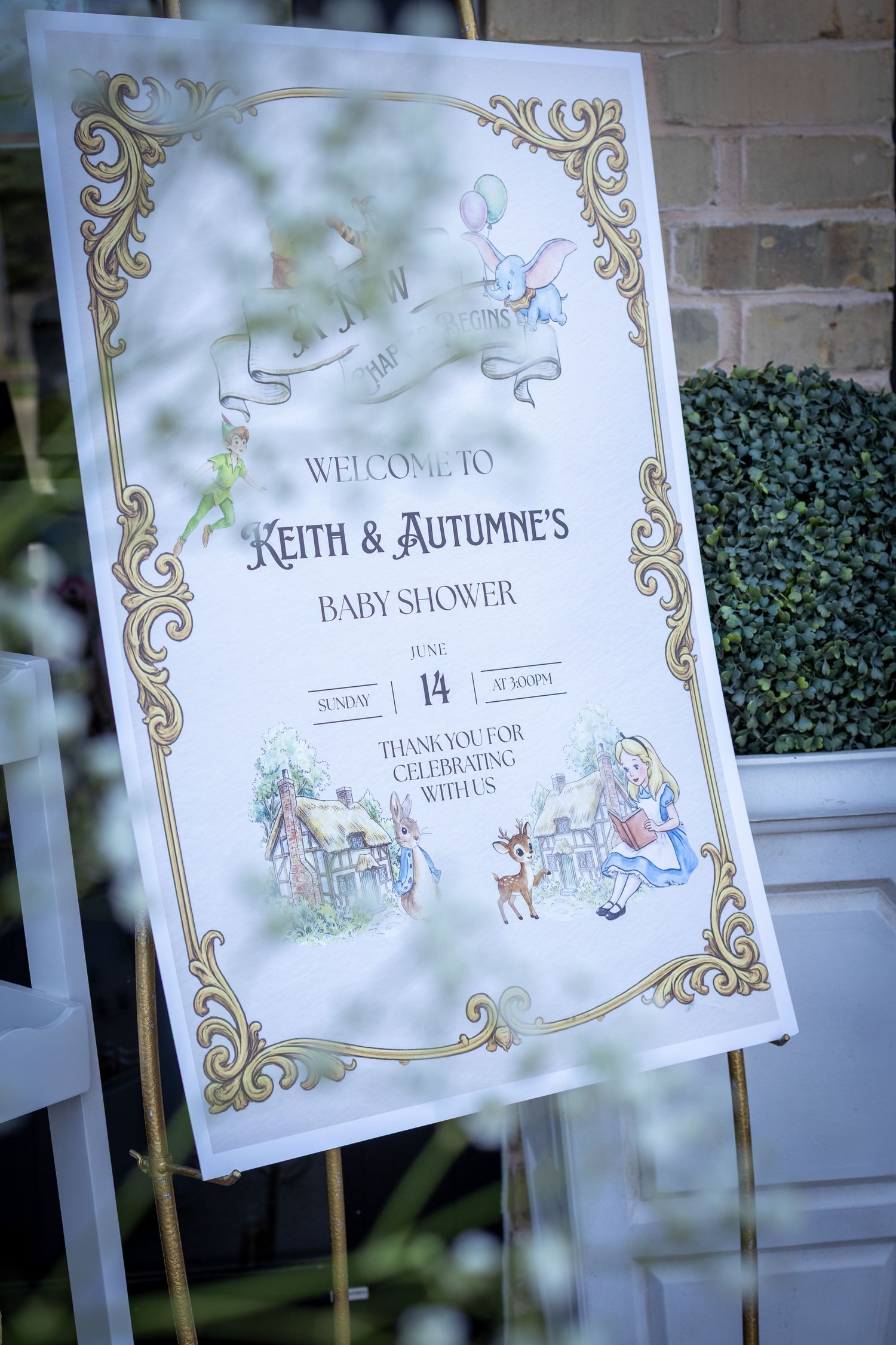 Elegant baby shower welcome sign for Keith & Autumne featuring gold borders and storybook illustrations on an easel.