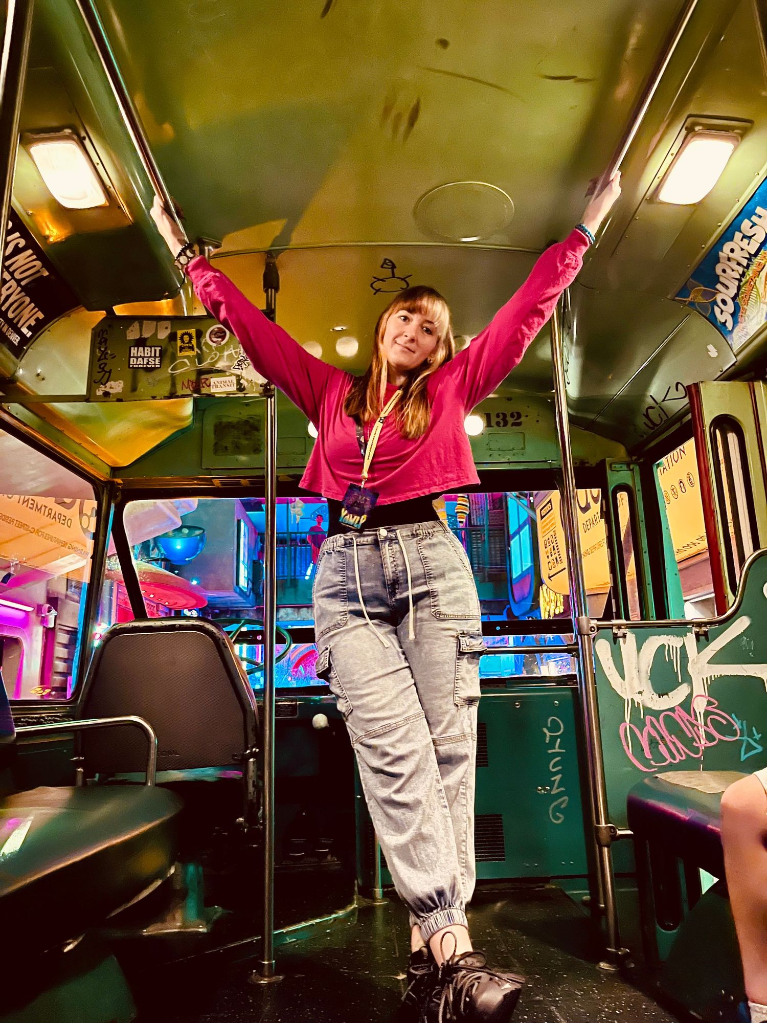 Young woman in pink hoodie and jeans poses on subway car handles, surrounded by colorful graffiti and arcade games.