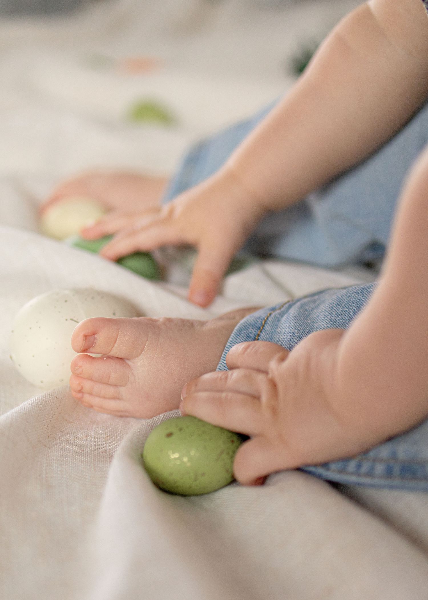 Baby hands and feet playing with green and white Easter eggs on a white blanket.
