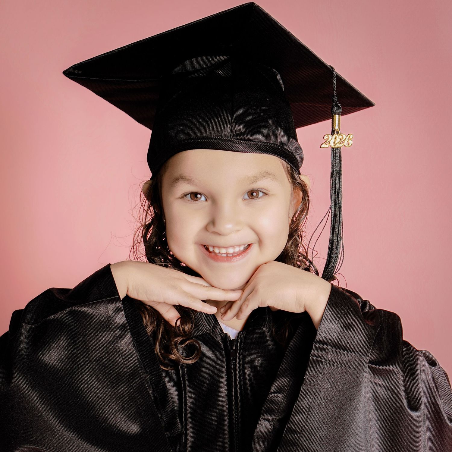 Young girl smiling in black graduation cap and gown for Pre-K ceremony.