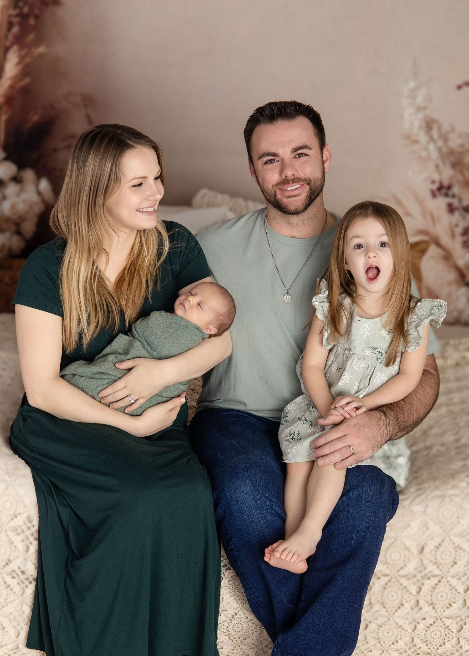 Family portrait on cream couch with newborn baby and young daughter in vintage setting.