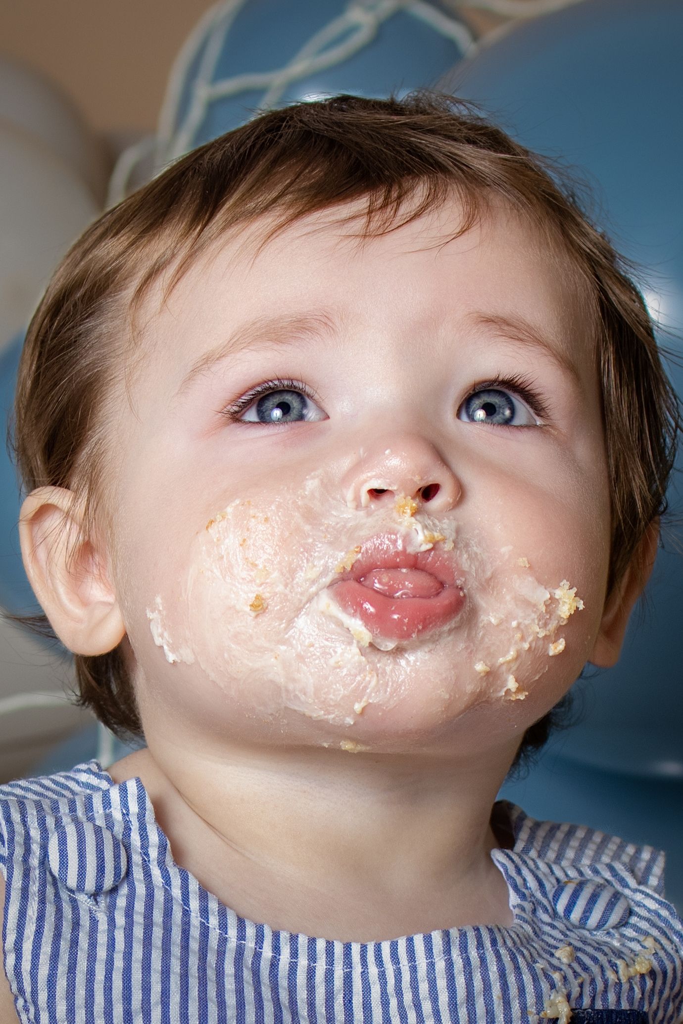 Adorable baby with blue eyes and cake smeared face enjoys first birthday cake smash celebration.