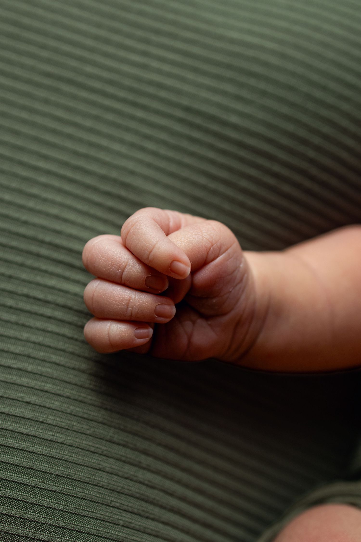 Close-up of a newborn baby's tiny clenched fist resting on a green ribbed fabric surface.
