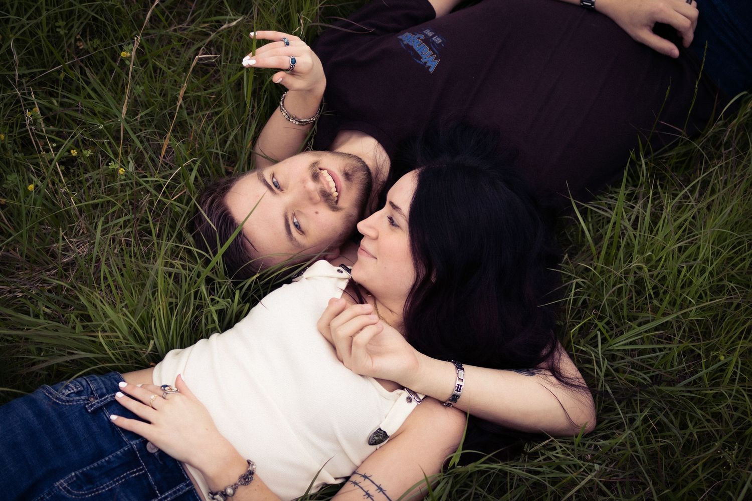 Three young women lying in green grass laughing and enjoying time together outdoors.