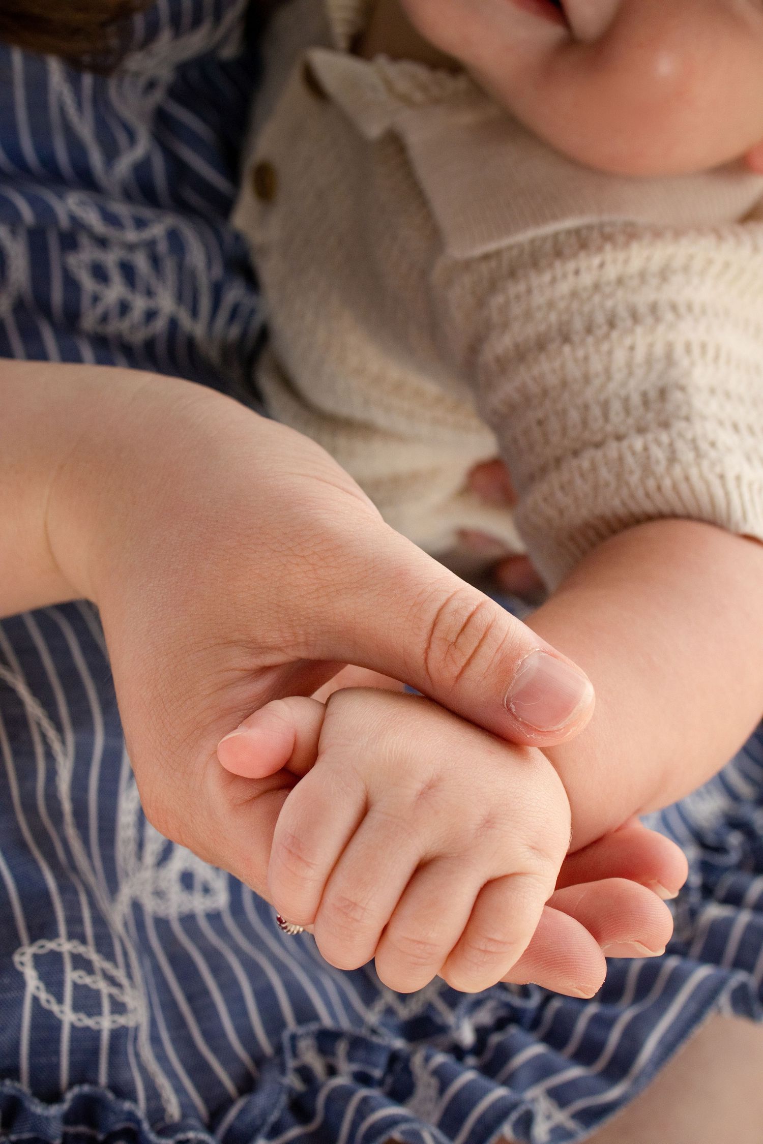 A mother gently holds her newborn baby's tiny hand, showcasing a tender bonding moment in soft natural light.