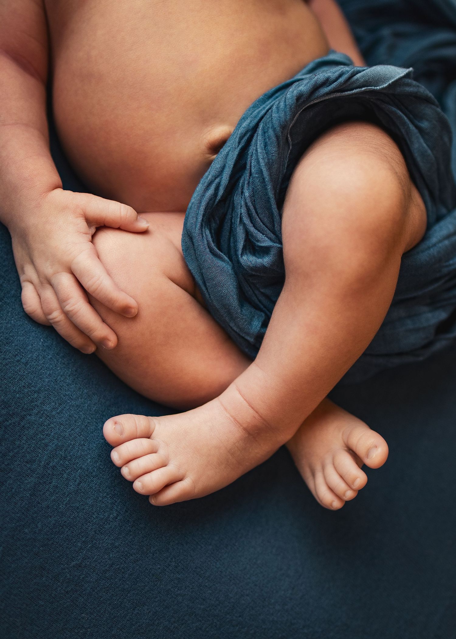 Close-up of a newborn baby's chubby legs and tiny toes wrapped in a soft blue cloth.